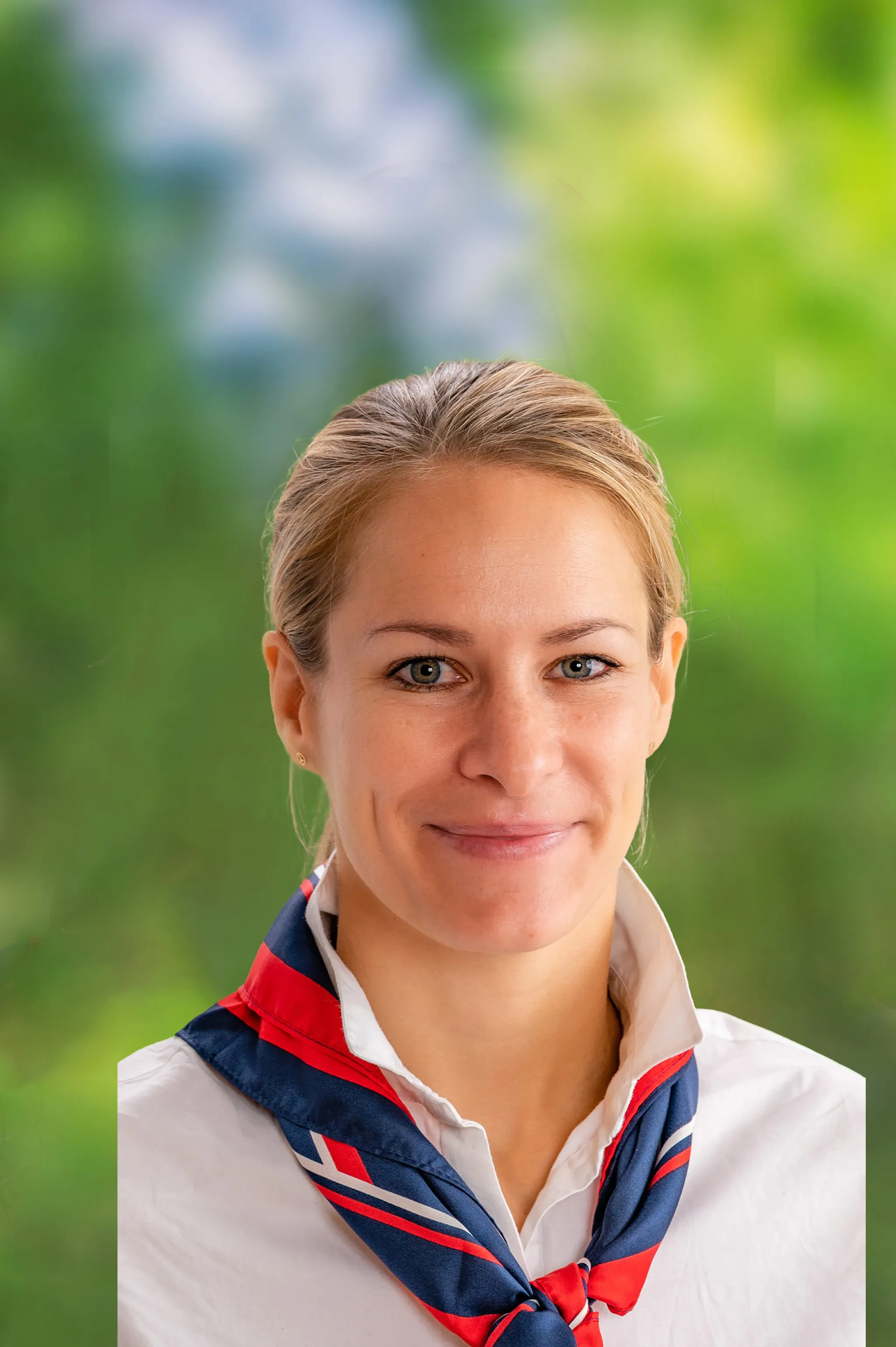 Frau mit einem leichten Lächeln, die eine weiße Bluse und ein blau‑rotes Tuch trägt.