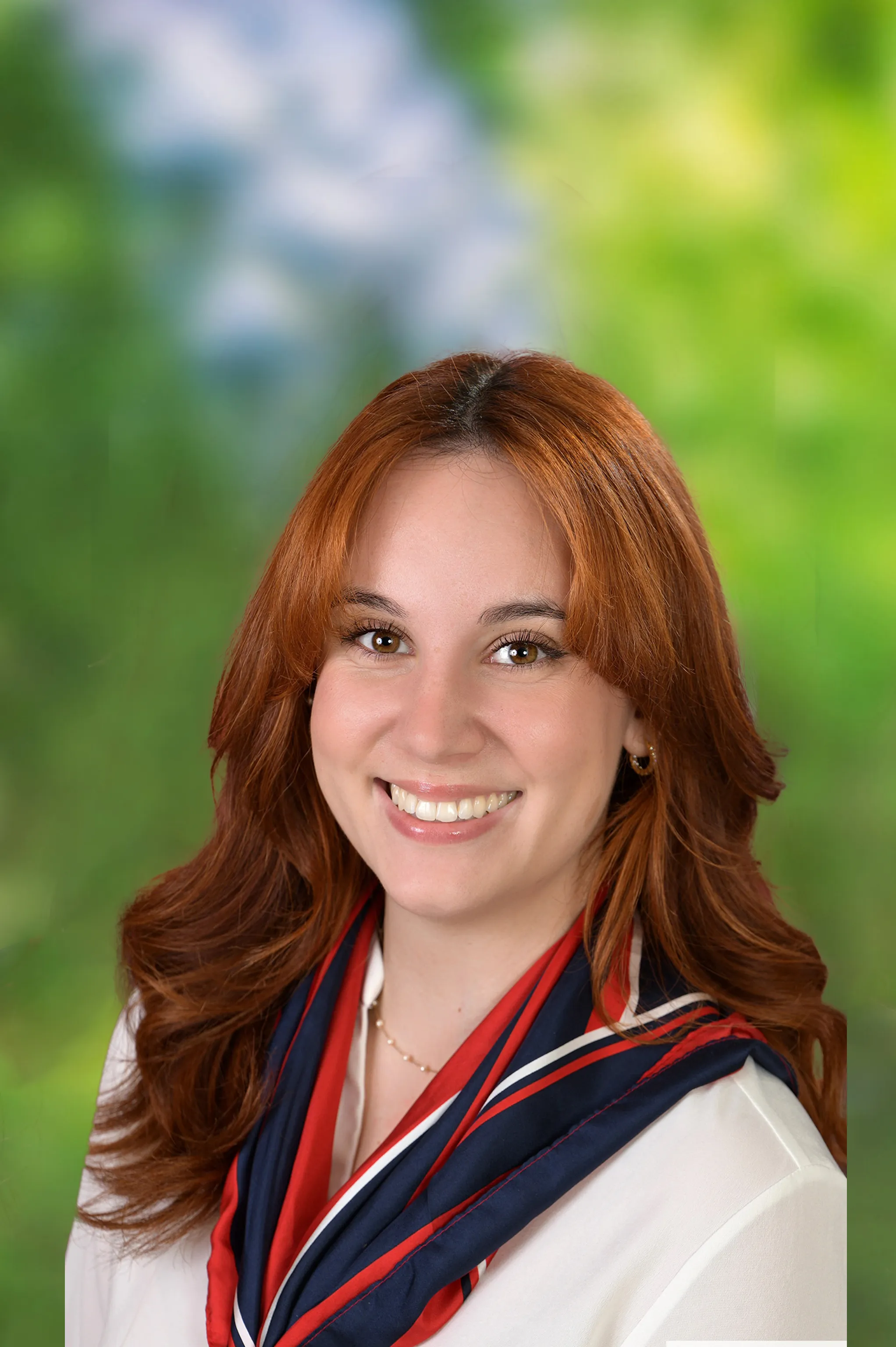 Lächelnde Frau mit kastanienbraunen Haaren, die ein rot-blaues Halstuch über einem weißen Oberteil trägt.