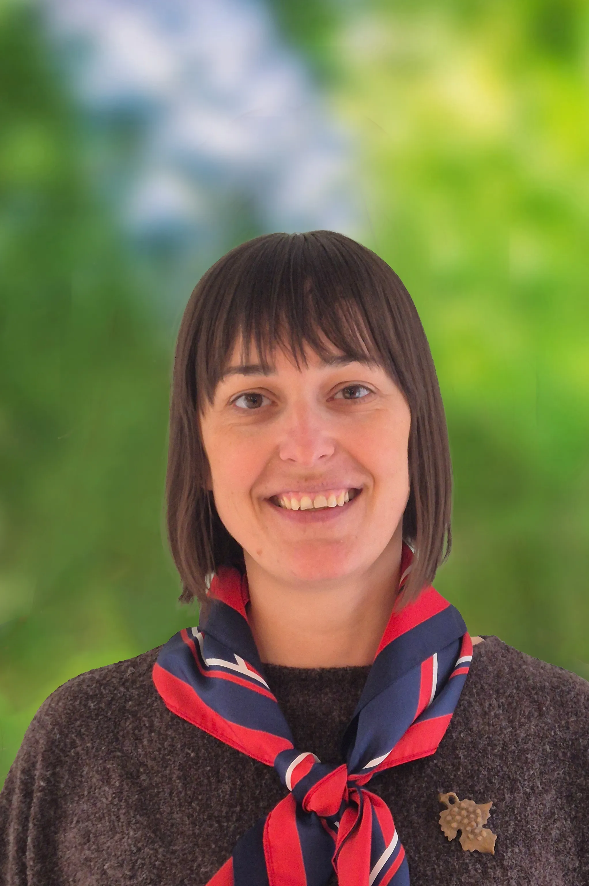 Lächelnde Frau mit schulterlangem Haar, die ein rot‑blaues Tuch und einen dunklen Pullover trägt.