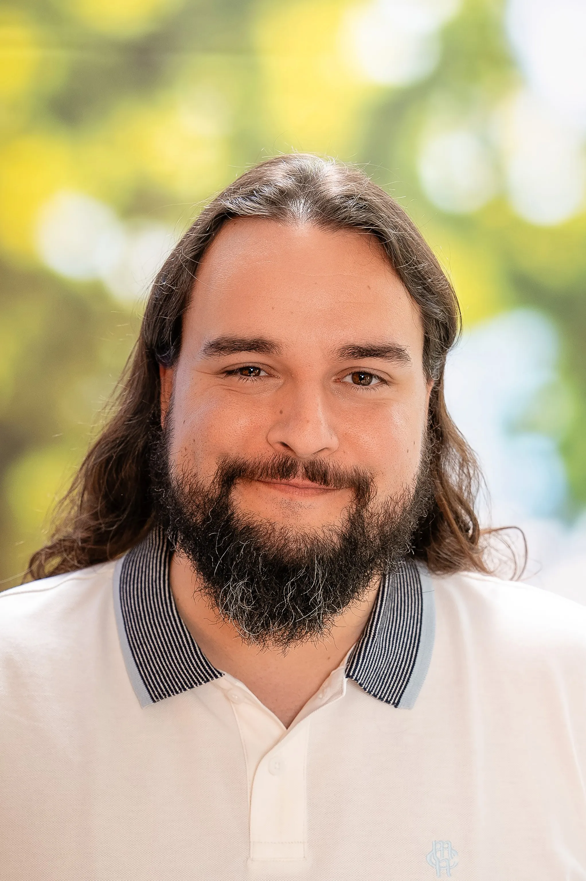 Ein Mann mit langen Haaren und Bart, der ein weißes Hemd mit Kragen trägt.