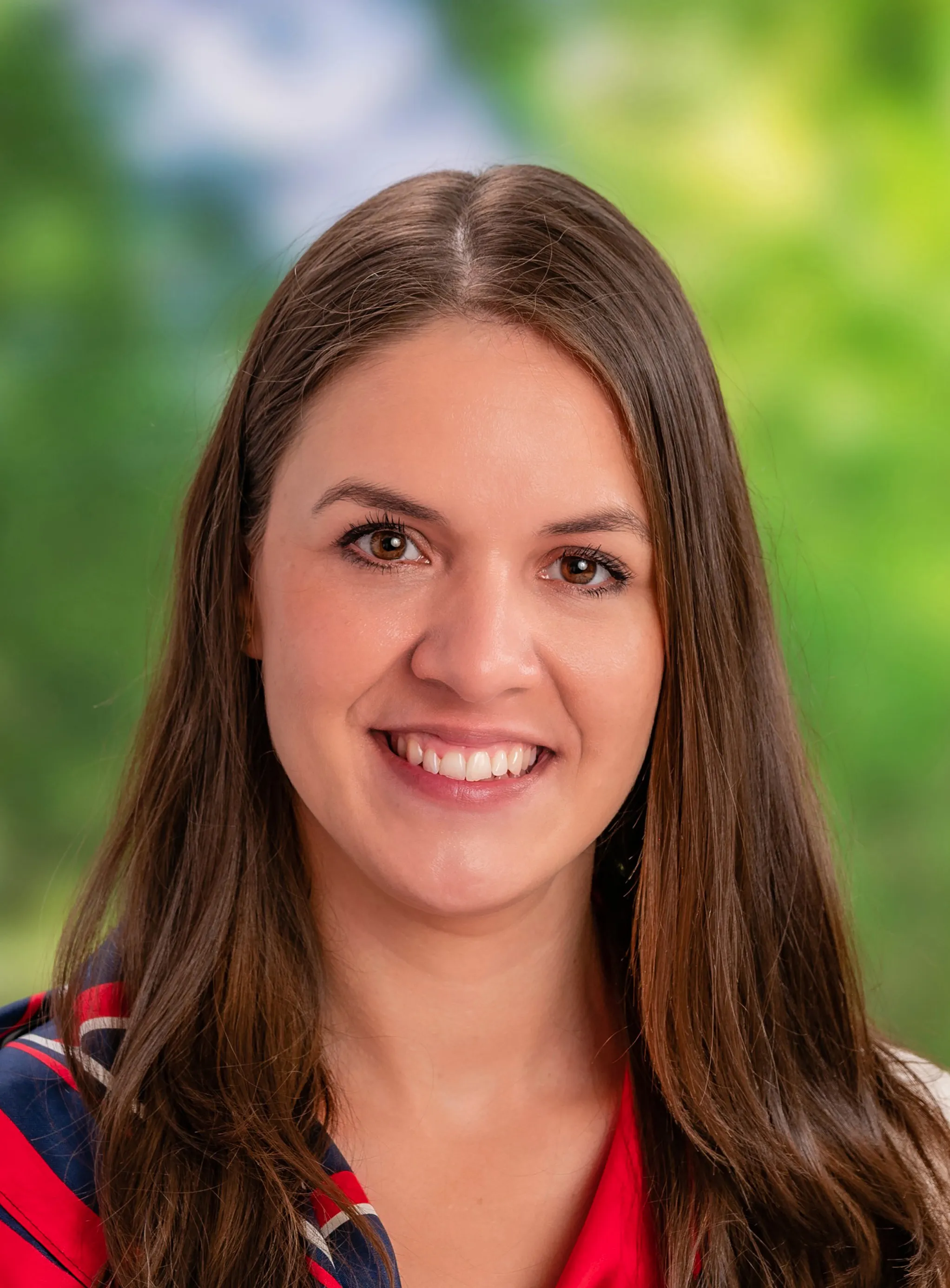 Frau mit langen braunen Haaren, die lächelt und ein rot‑blaues Halstuch trägt.