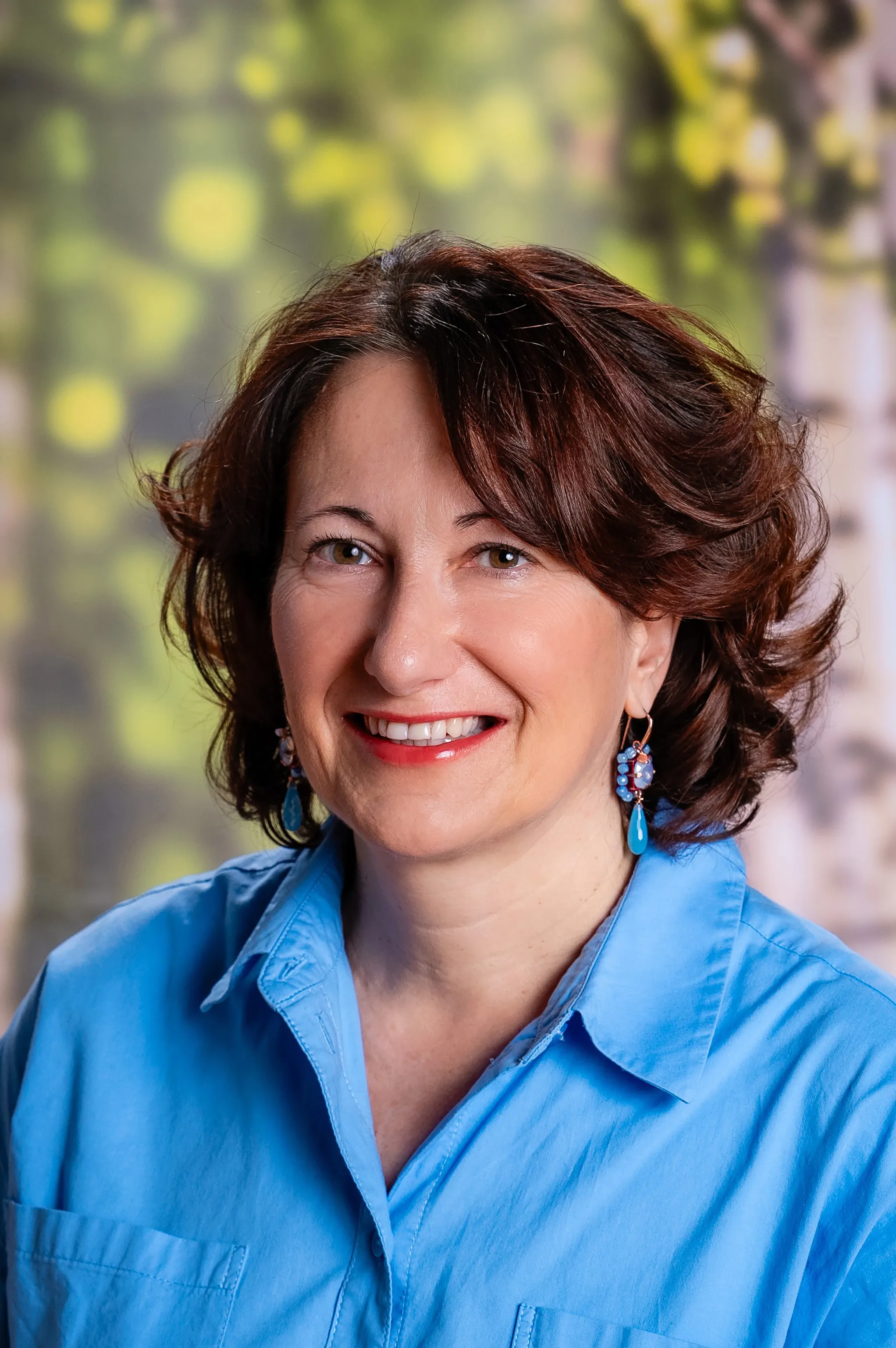 Portraitfoto einer Frau mit strahlendem Lachen, kurzen braunen Haaren und einer blauen Bluse