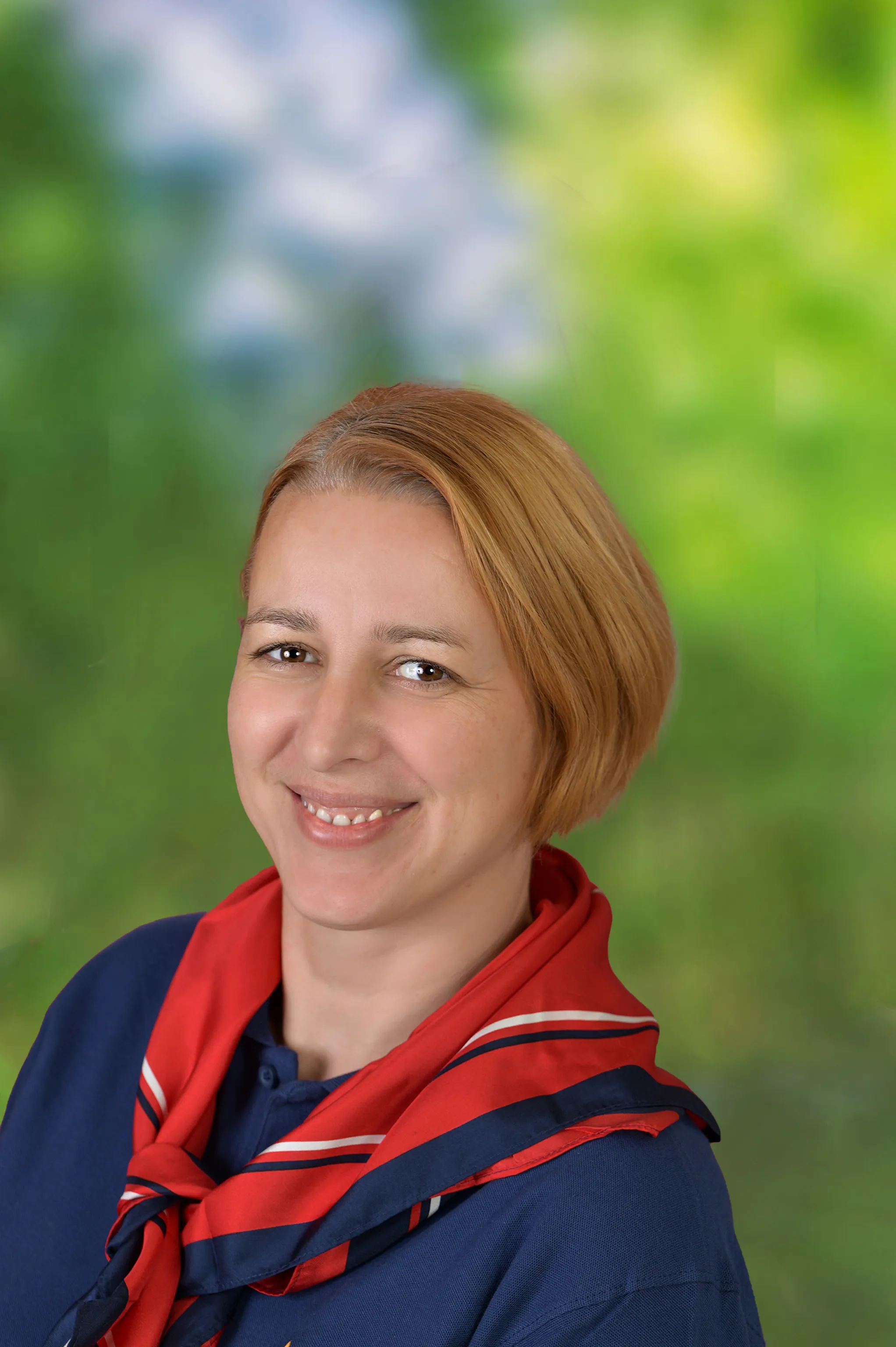 Lächelnde Person mit kurzen rot-blonden Haaren, die ein blaues Shirt und ein rot-blaues Halstuch trägt.