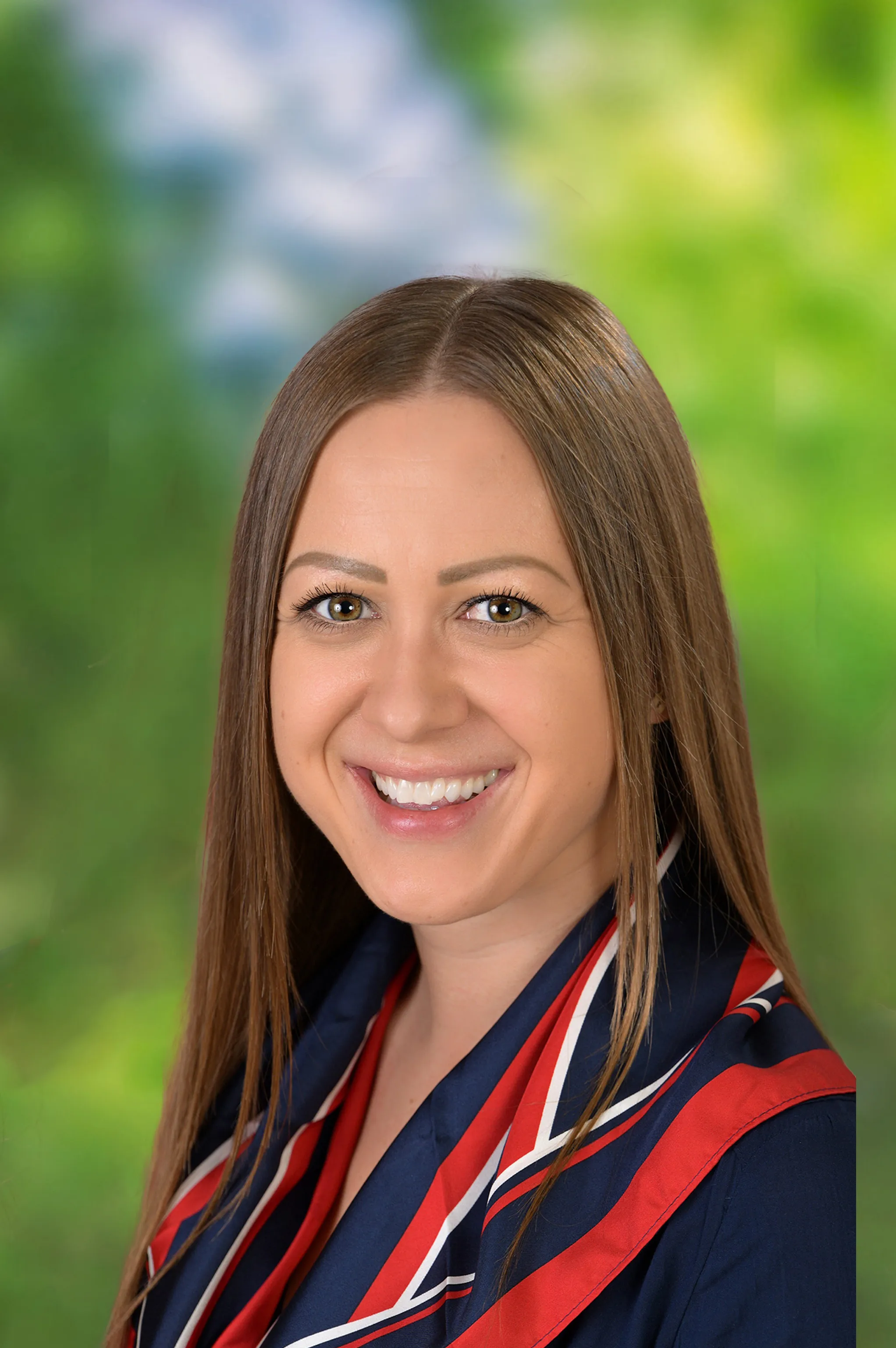 Lächelnde Frau mit langen braunen Haaren, die ein blau-rotes Halstuch trägt.