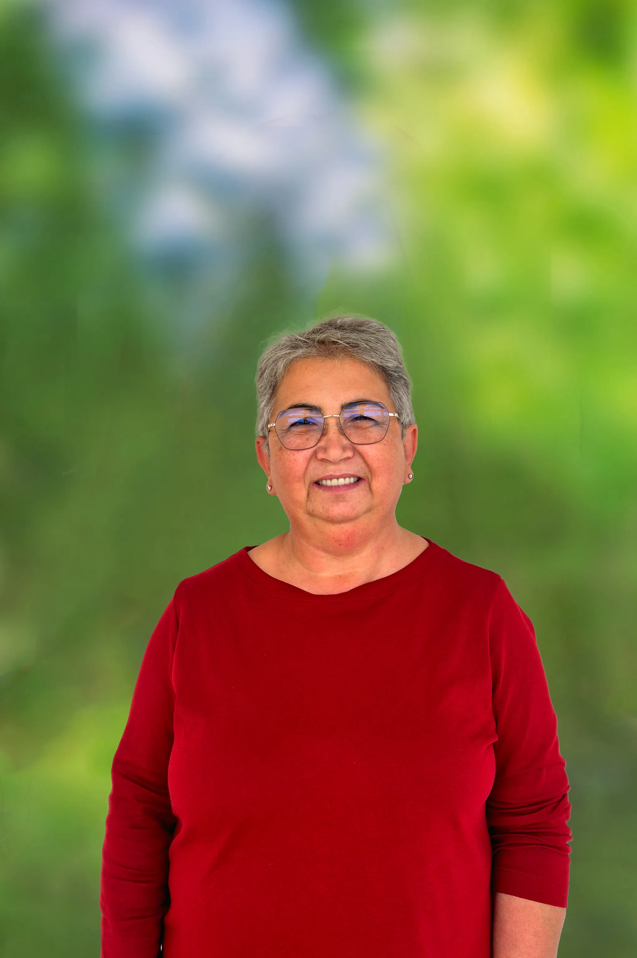 Freundlich lachende Dame mit kurzen grauen Haaren und Brille mit Ohrsteckern und rotem Pullover.