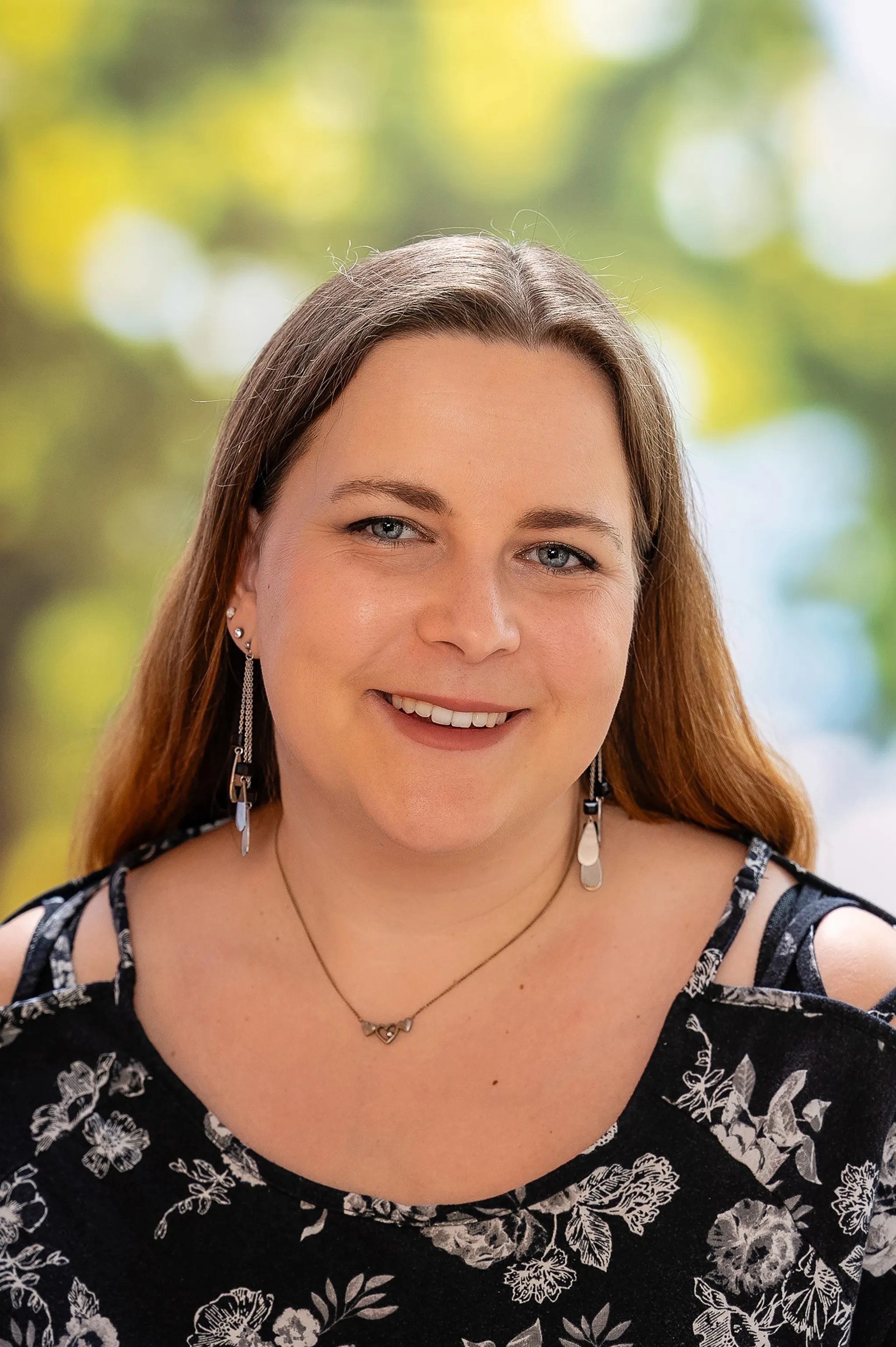 Eine lächelnde Frau, die ein geblümtes Oberteil, eine Kette und Ohrringe trägt