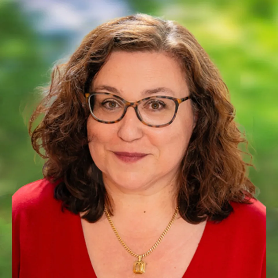Eine Frau mit braunem gelpcktem Haar, Brille, einen roten Pullover und einer Halskette.