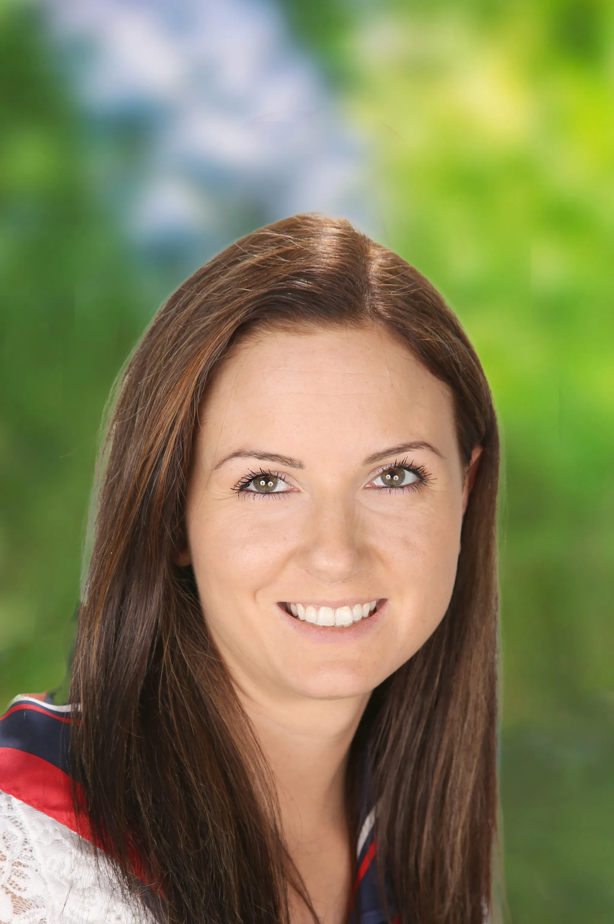 Lächelnde Frau mit langen braunen Haaren, die ein weißes Oberteil und ein rot‑blaues Tuch trägt.