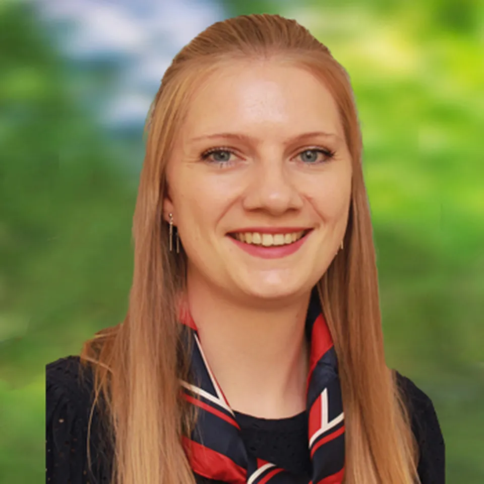 Lächelnde Frau mit langem blondem Haar, die ein schwarzes Oberteil und ein rot‑weiß‑blaues Tuch trägt.