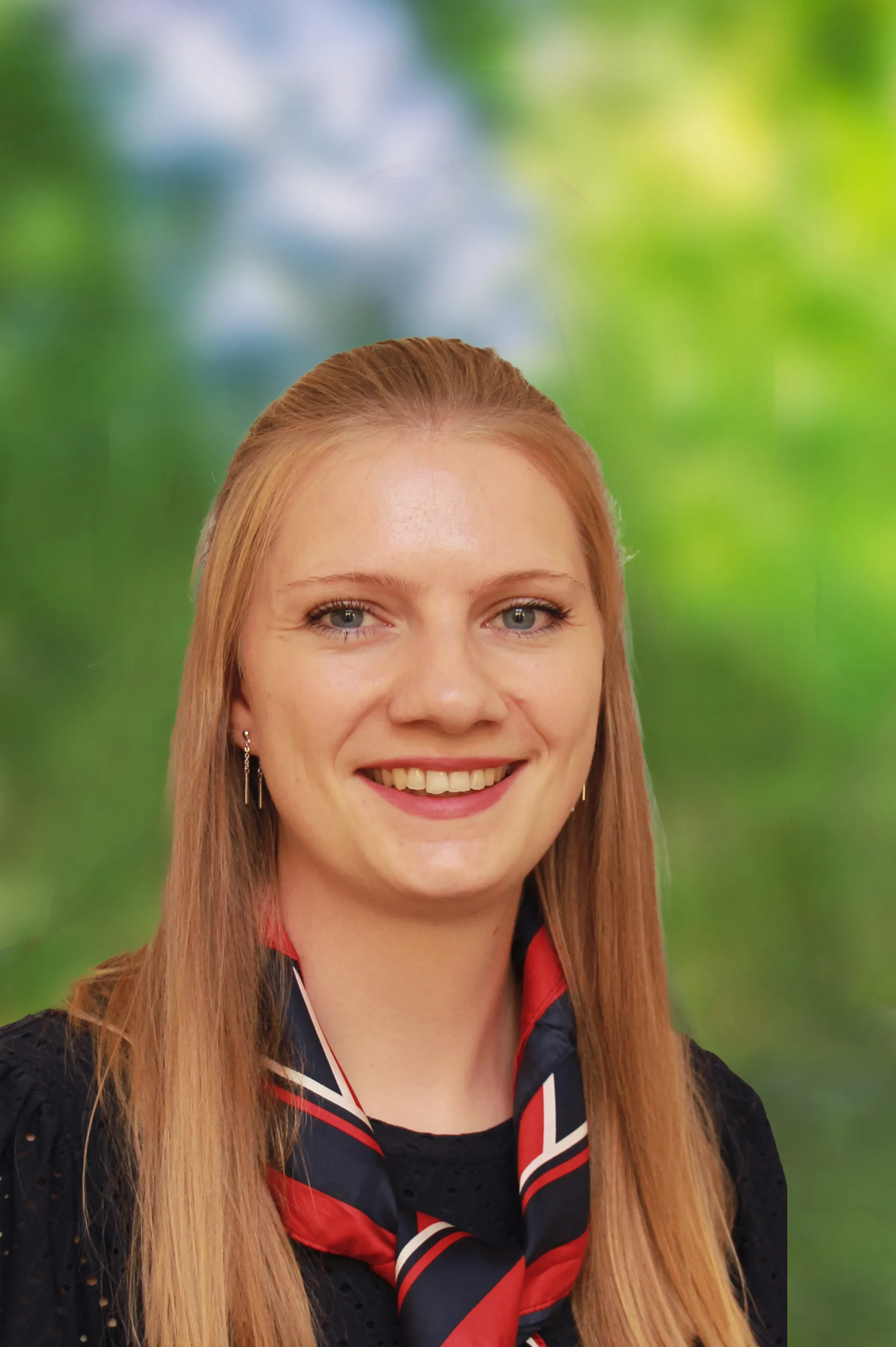 Lächelnde Frau mit langem blondem Haar, die ein schwarzes Oberteil und ein rot‑weiß‑blaues Tuch trägt.