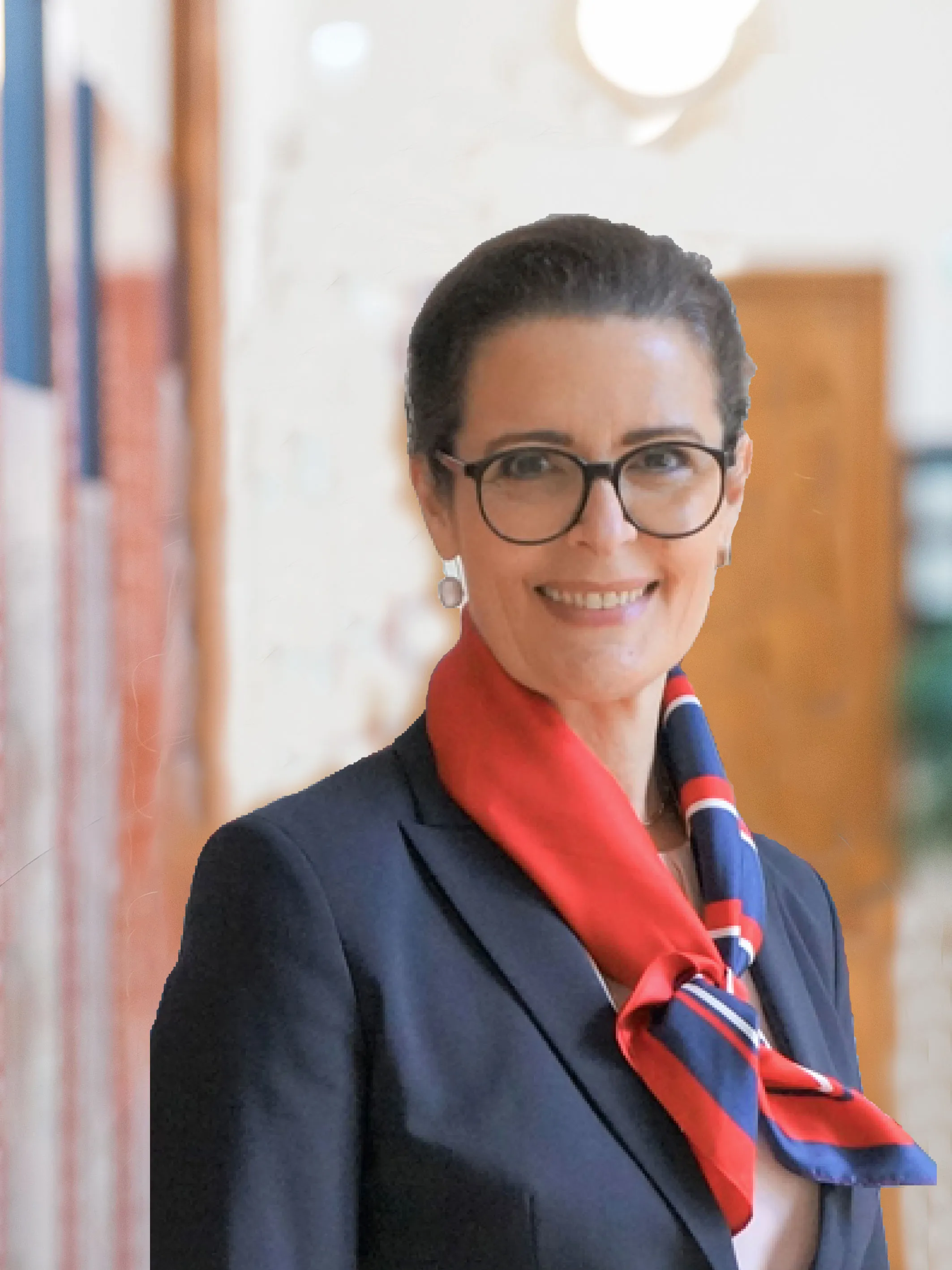 Frau mit dunkler Brille und glatt nach hinten frisierten dunklen Haaren mit eleganter dunkelblauer Jacke und rot blau weißem Seidentuch