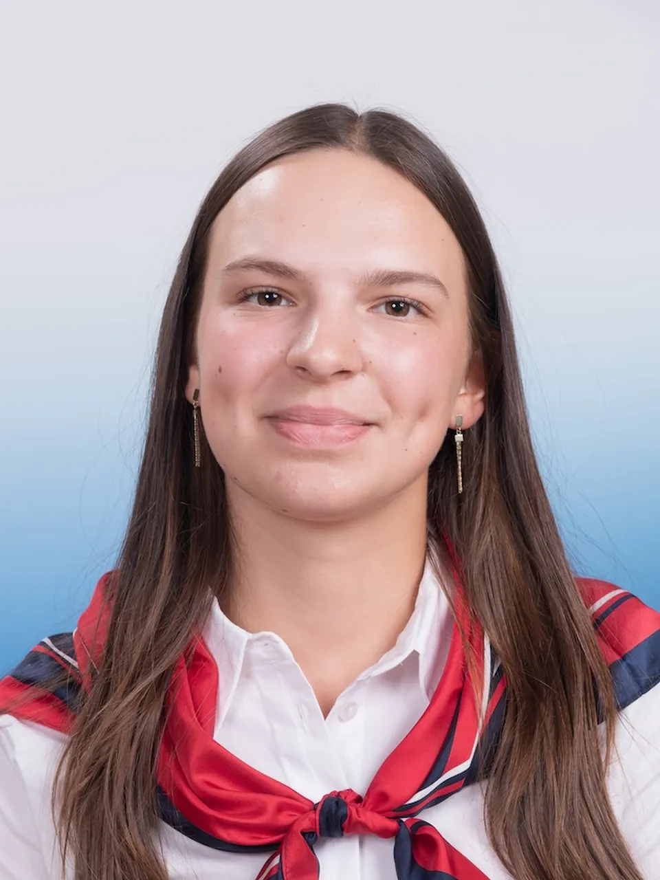 portraitfoto einer frau mit langen brünetten Haaren und mit freundlichem lachen in die kamera blickend, elegante Ohrringe, eine weiße Bluse und ein rot blaues Seidentuch tragend