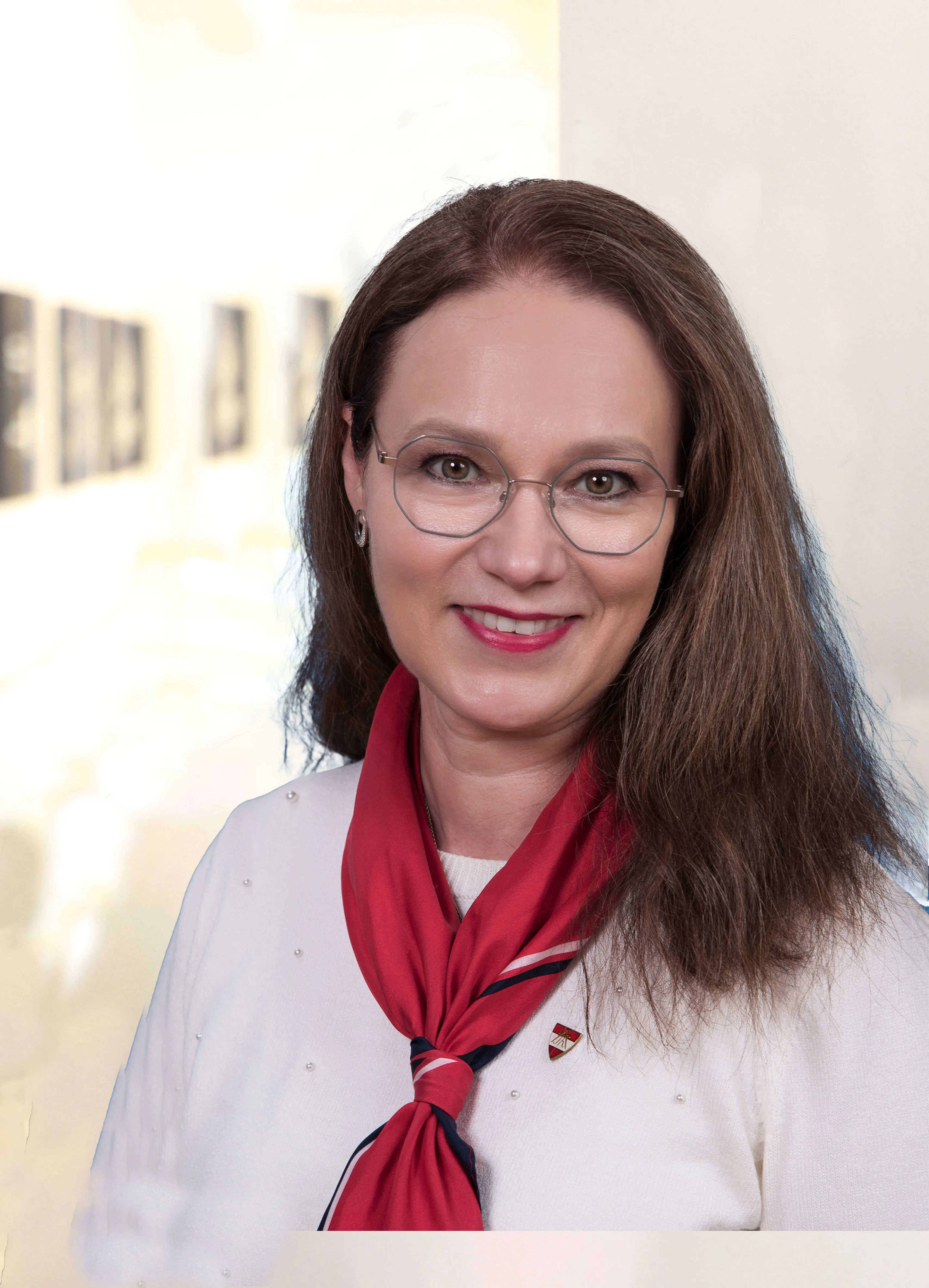 Portrait einer Frau mittleren Alters mit braunen langen Haaren, rotem Lippenstift, freundlichem Lachen und rotem Seidenhalstuch