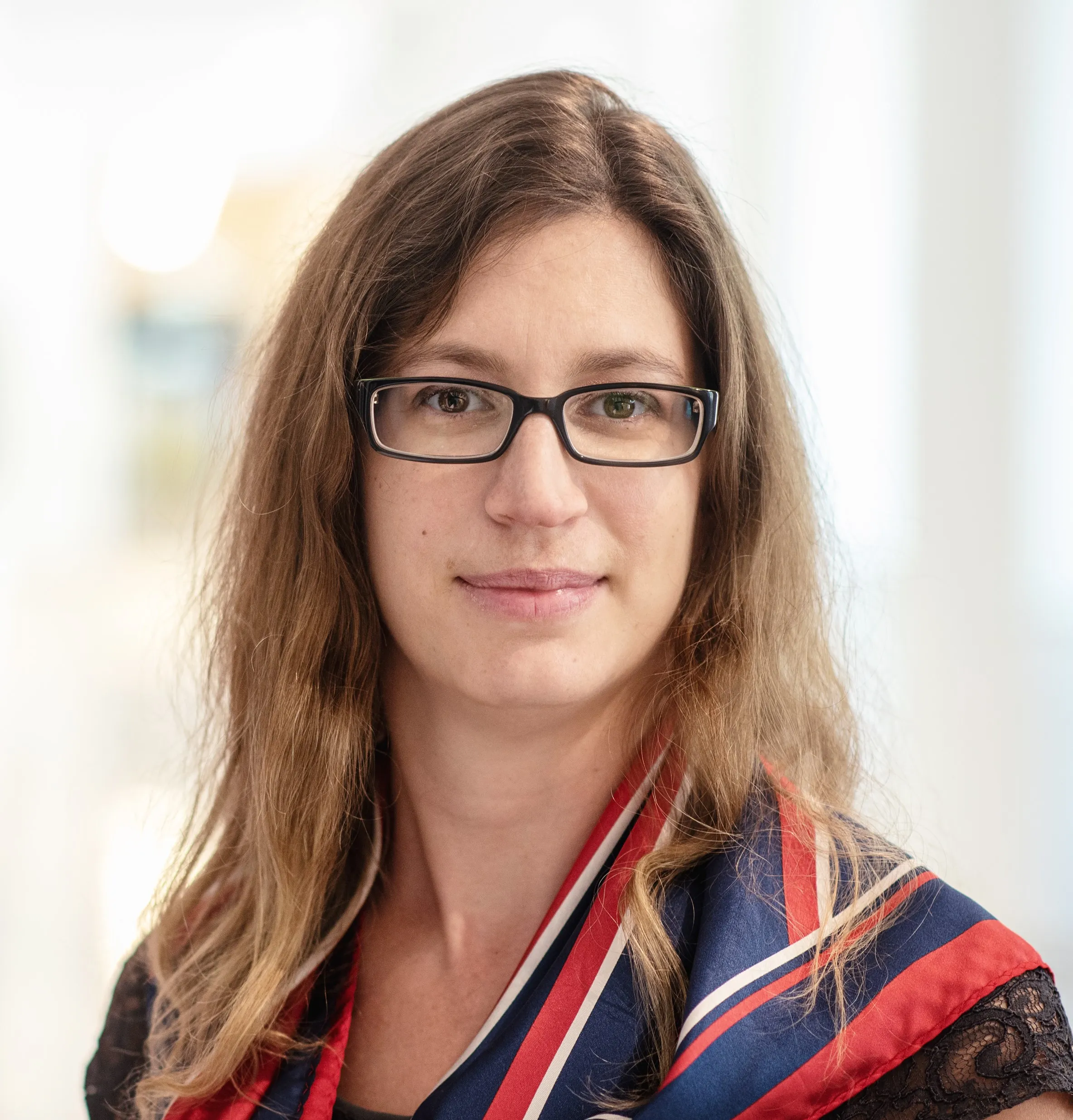 Frau mit brünettem langen Haar, die eine Brille und das rot-blaue Theresianum Tuch trägt.