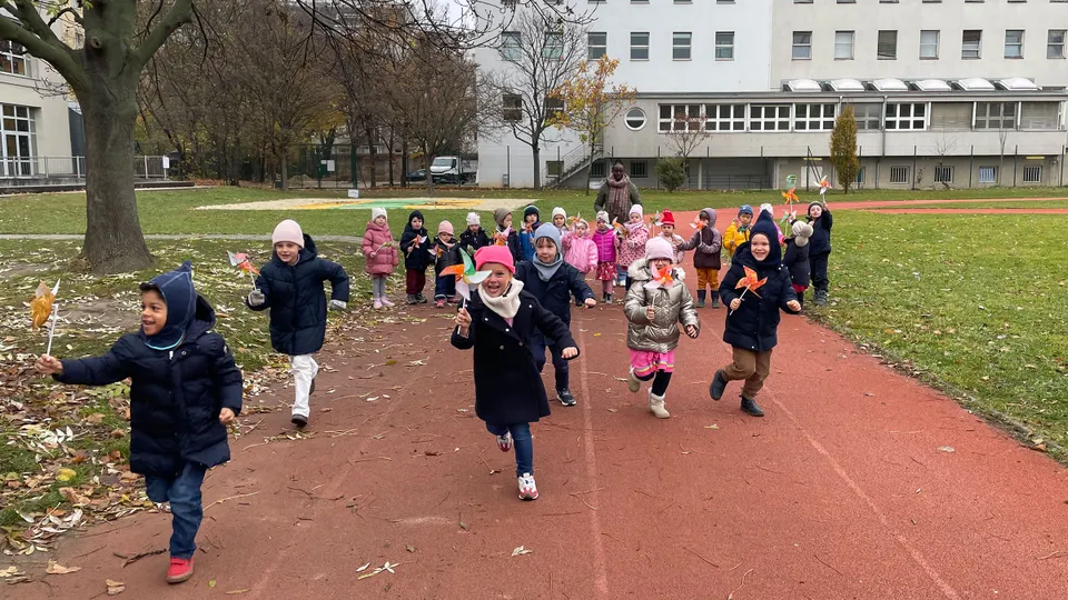 Gruppe von Kinder im Herbst mit Windrädchen über eine Laufbahn flitzend.