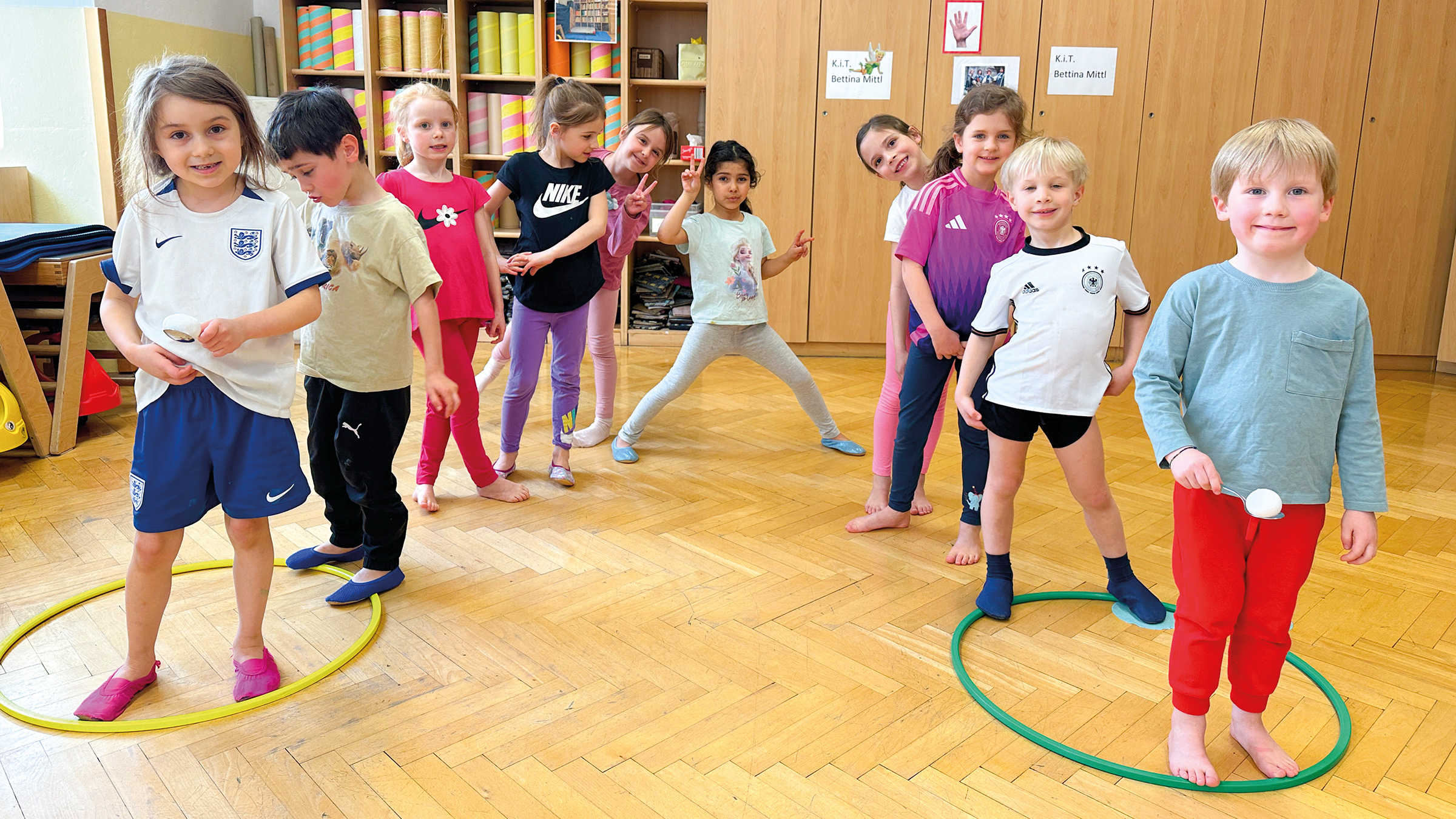 Gruppe von Vorschulkindern in Turnkleidung in zwei Reihen locker hintereinander stehend und die ersten beiden Buben jeweils mit Löffel und Ei in der Hand auf ein Startsignal wartend.