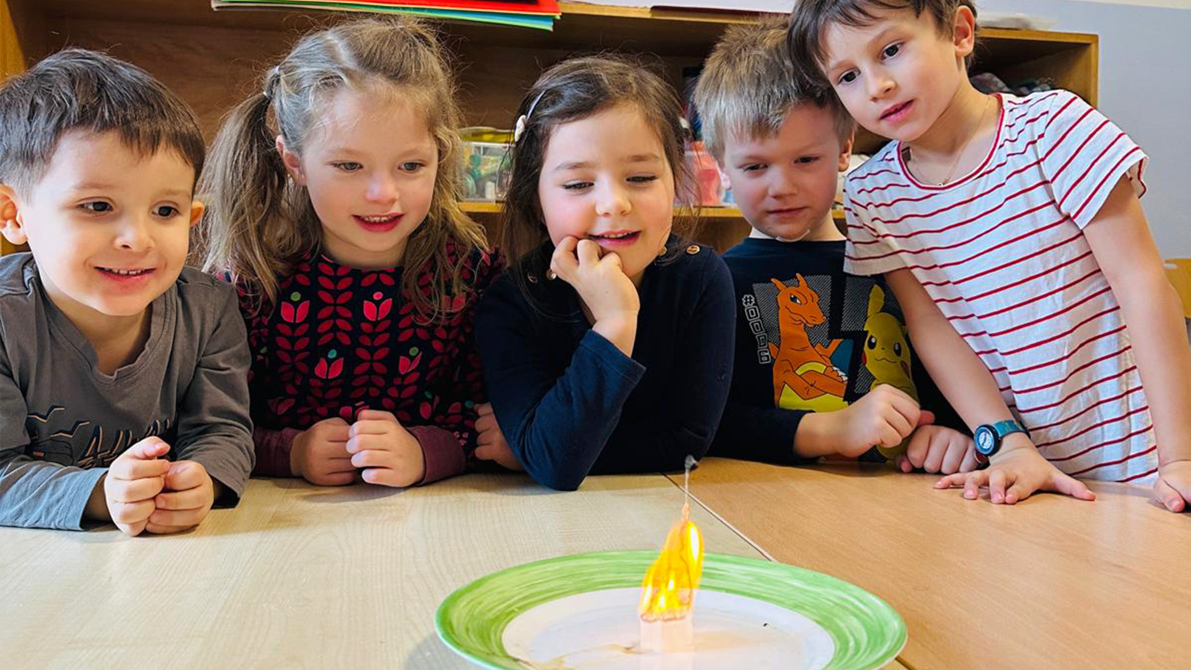Gruppe von fünf Kleinkindern die fasziniert und begeistert auf eine vor ihnen stehende Flamme schauen.