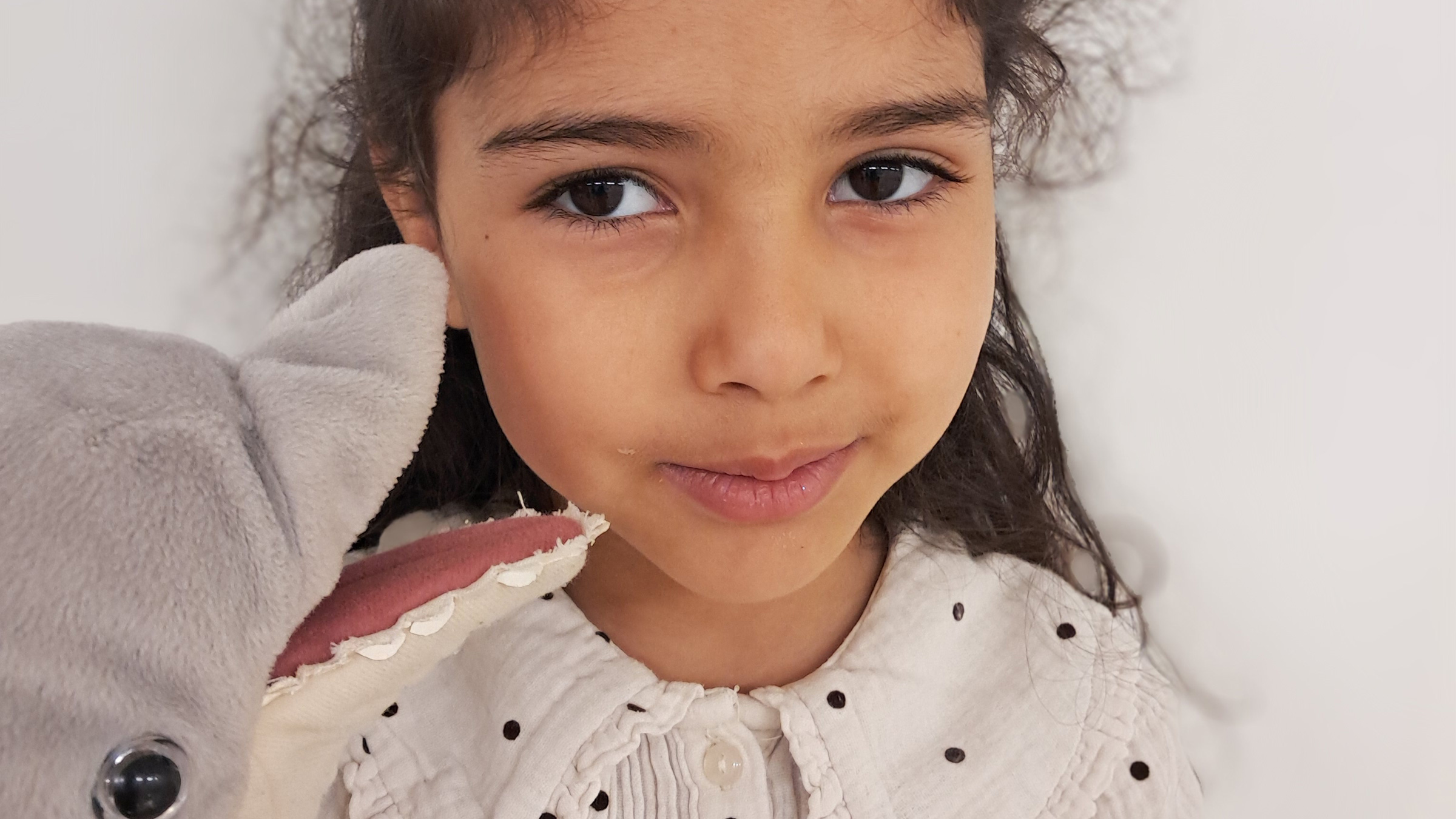 Close up eines Mädchens mit Kuscheltier in der Hand schüchtern in die Kamera blickend.