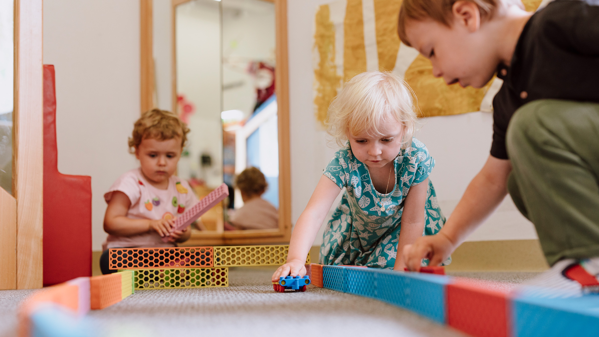 Drei kleine Kinder am Boden mit Bausteinen und Autos spielend