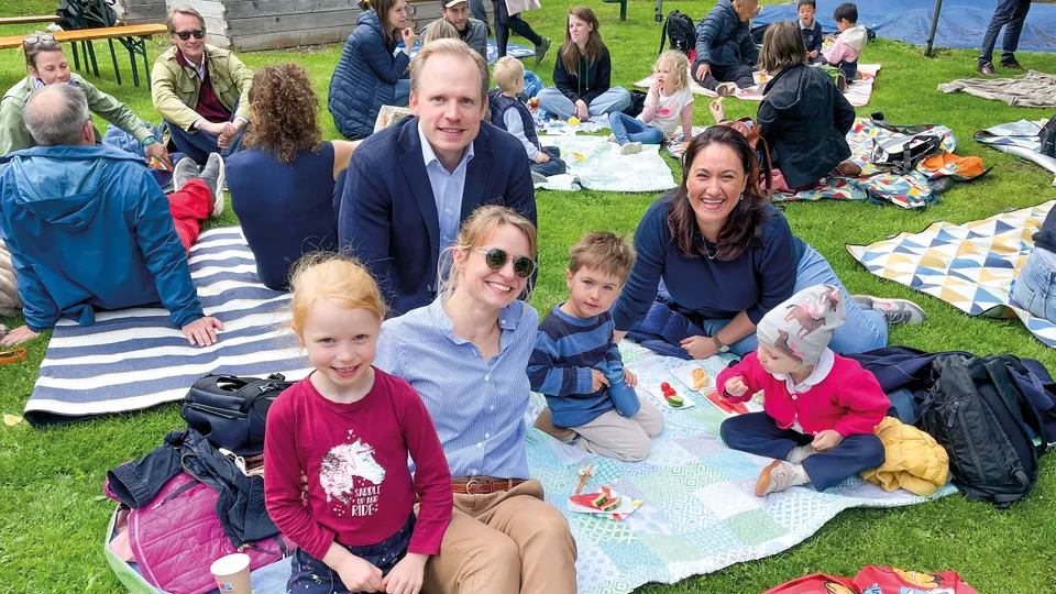 Erwachsene Menschen und Kinder verschiedenen Alters gemütlich und gut gelaunt auf Picknickdecken auf einer Wiese sitzend