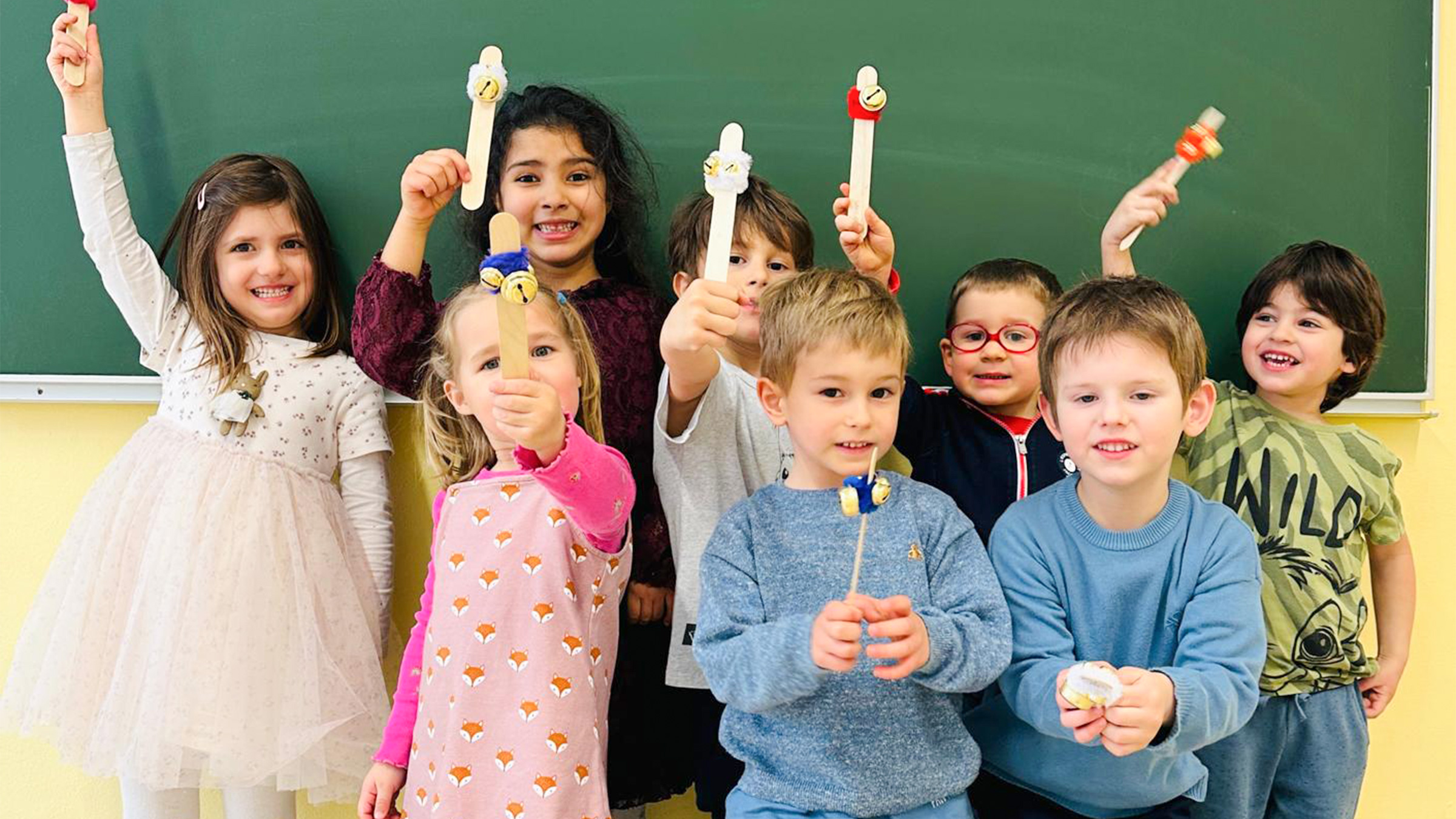 Gruppe von Kindern vor einer grünen Schultafel stehend, die selbstgebastelte Musikstöckchen stolz herzeigen