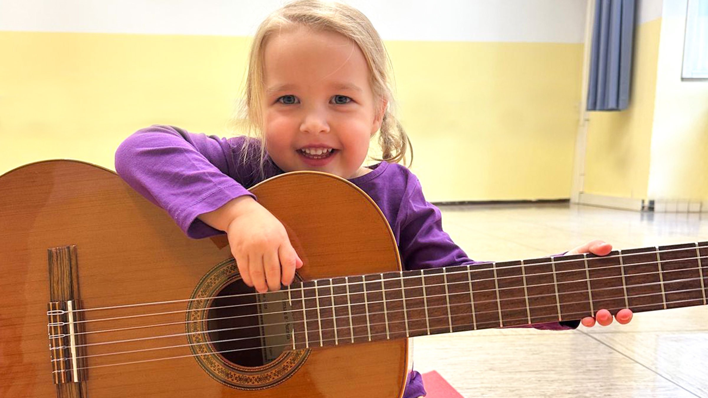 Blondes lachendes Mädchen mit großer Gitarre in den Händen