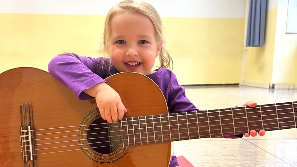 Blondes lachendes Mädchen mit großer Gitarre in den Händen