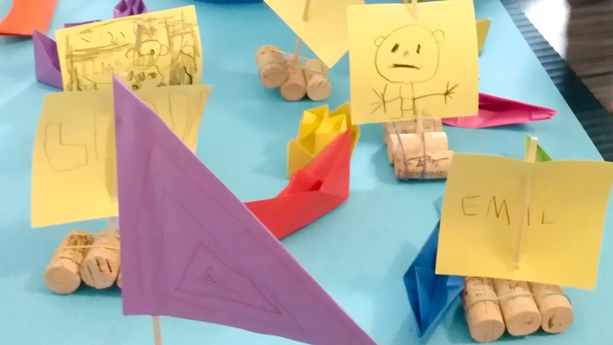 Kleine Flosse aus Kork mit gelben Papiersegeln und bunten Papierschiffchen.