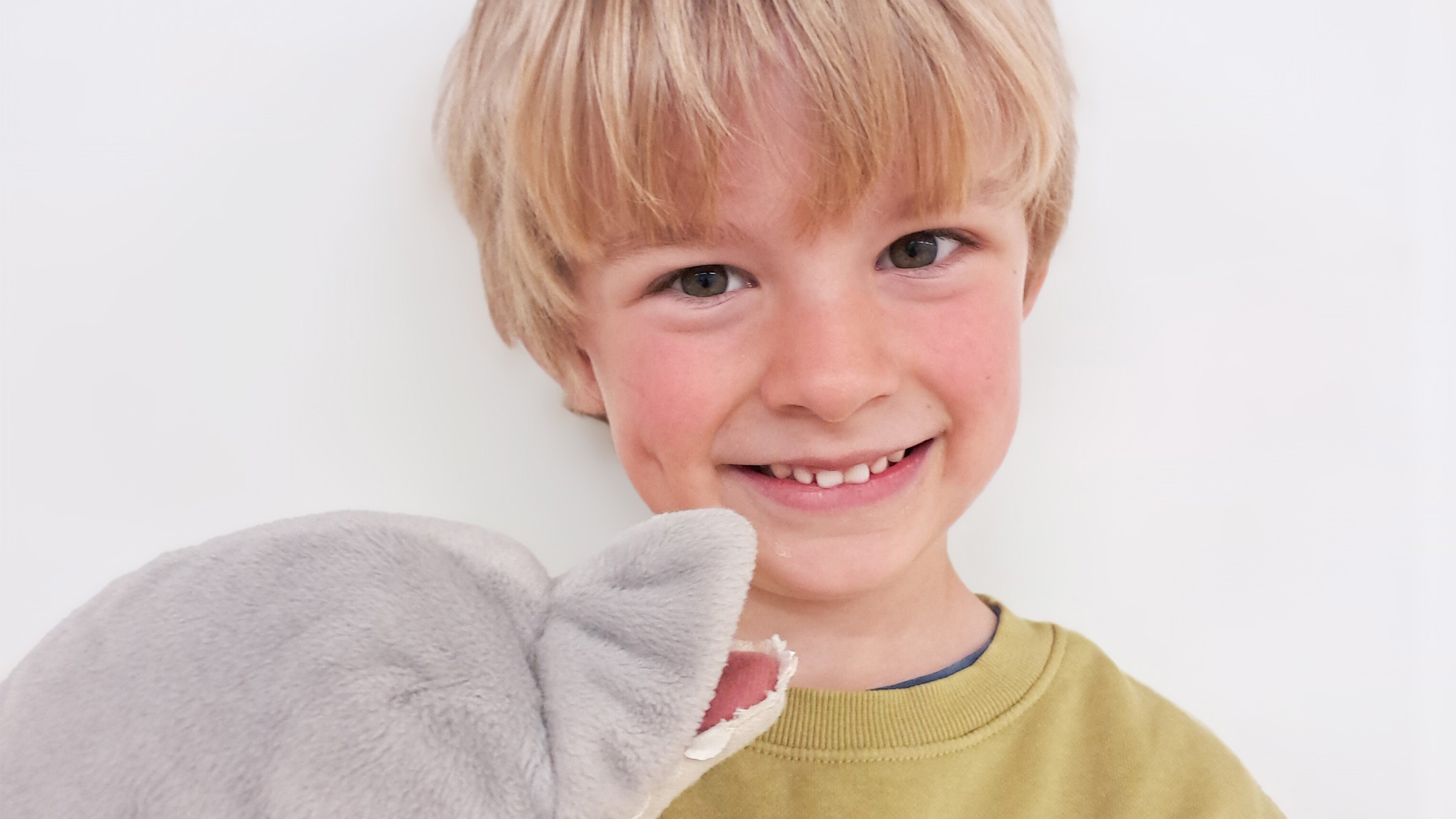 Blonder Bub mit Kuscheltier in die Kamera lachend