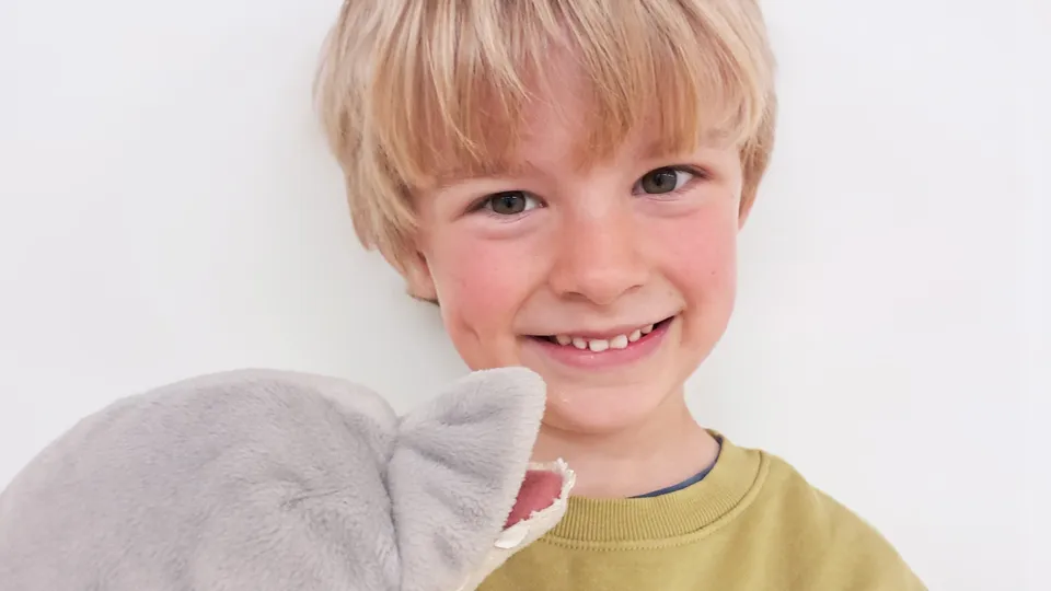 Blonder Bub mit Kuscheltier in die Kamera lachend