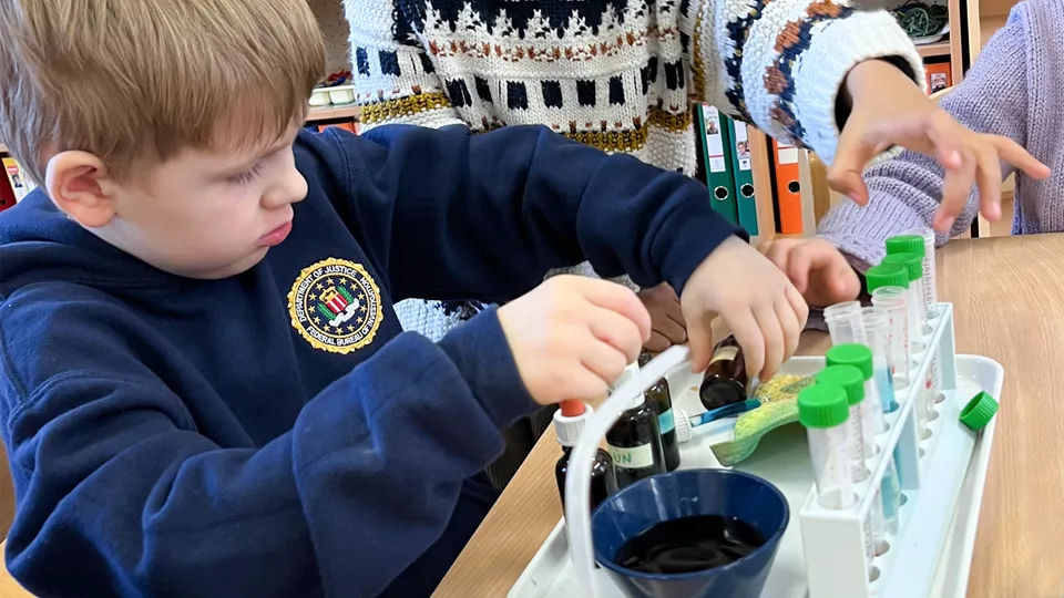 Junger Bub mit blauem Pullover mit Pipetten und Chemikalien arbeitend.