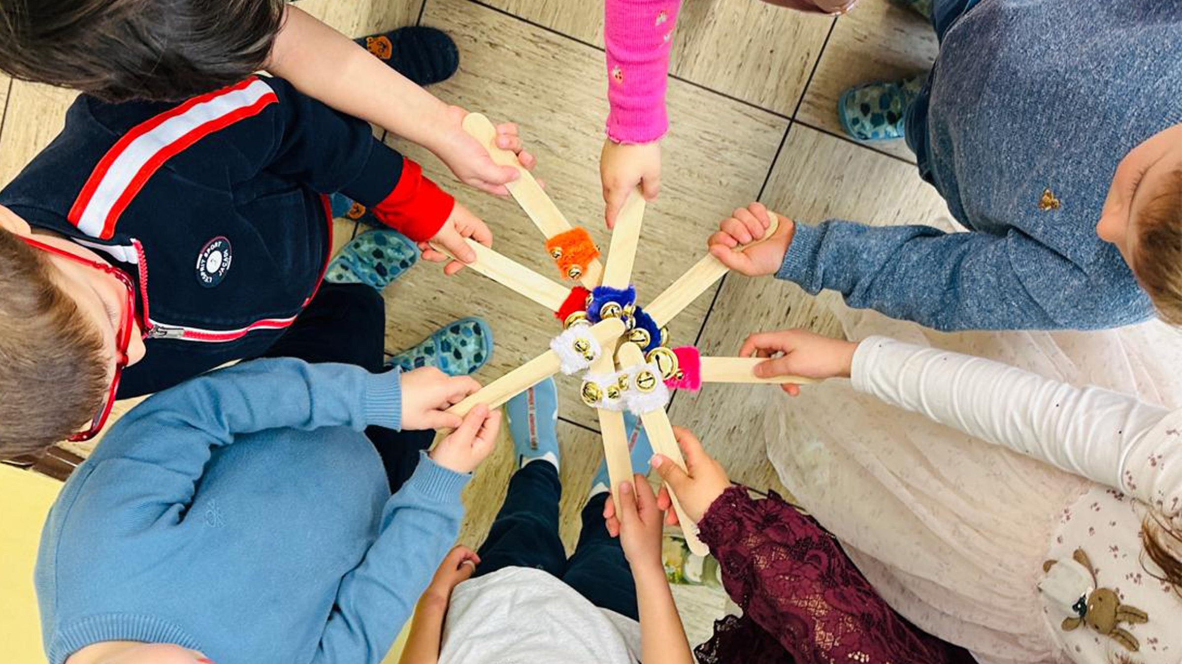 Blick von oben auf eine Gruppe von Kindern die selbstgebastelte Musikstöckchen in einem Kreis zusammenstoßen lassen