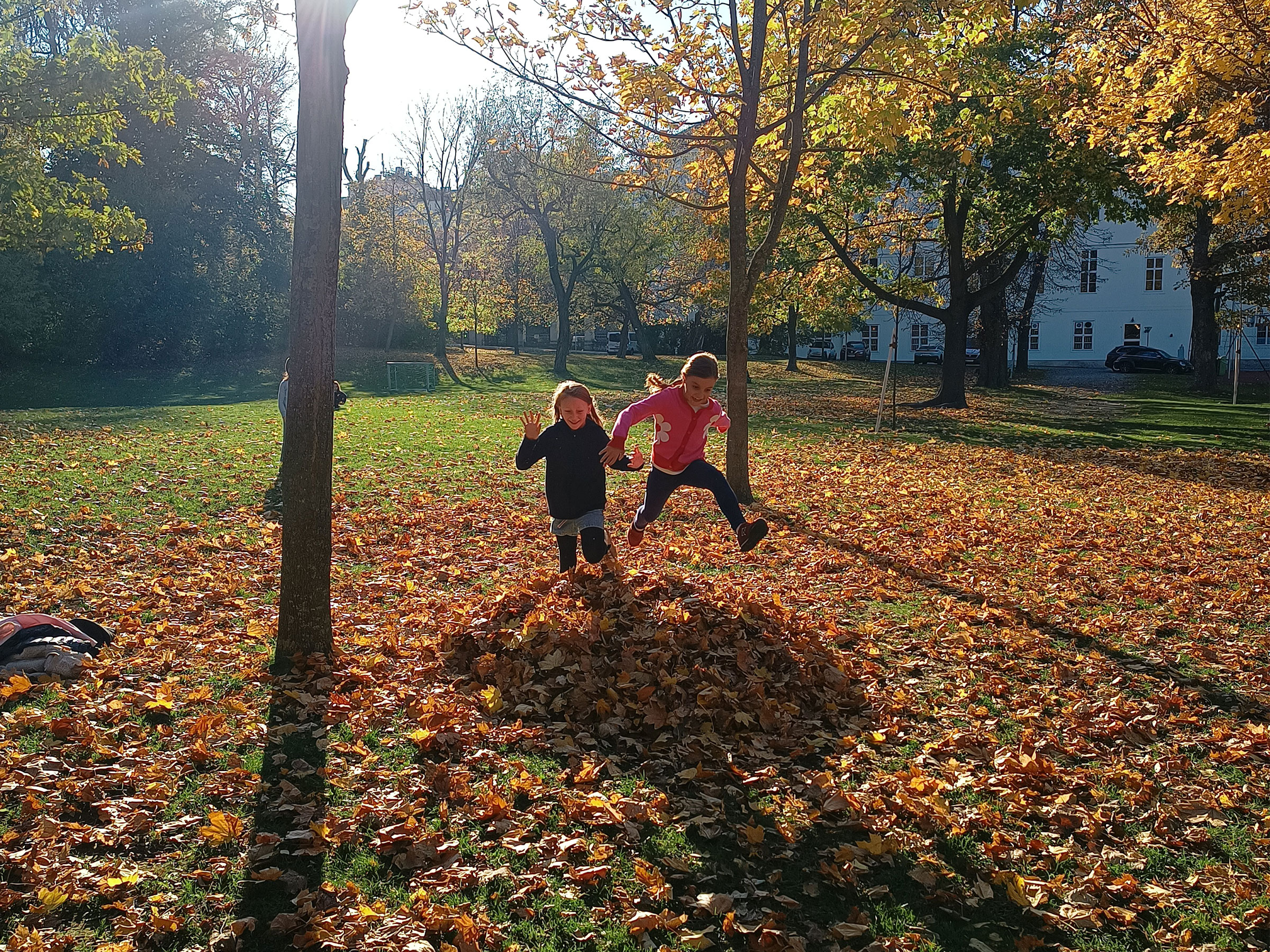 Zwei Mädchen bei sonnigem Herbstwetter in einem Park in einem Laubhaufen springend