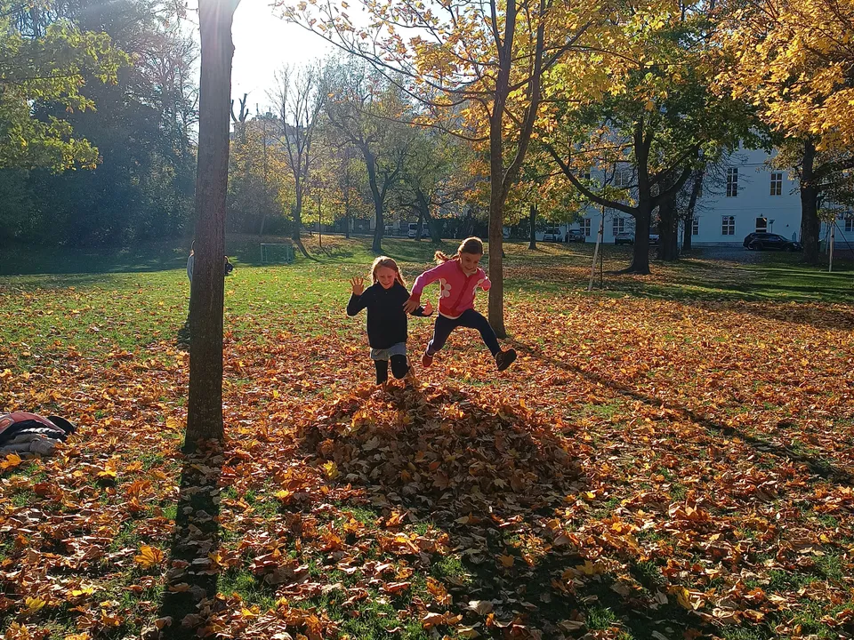 Zwei Mädchen bei sonnigem Herbstwetter in einem Park in einem Laubhaufen springend