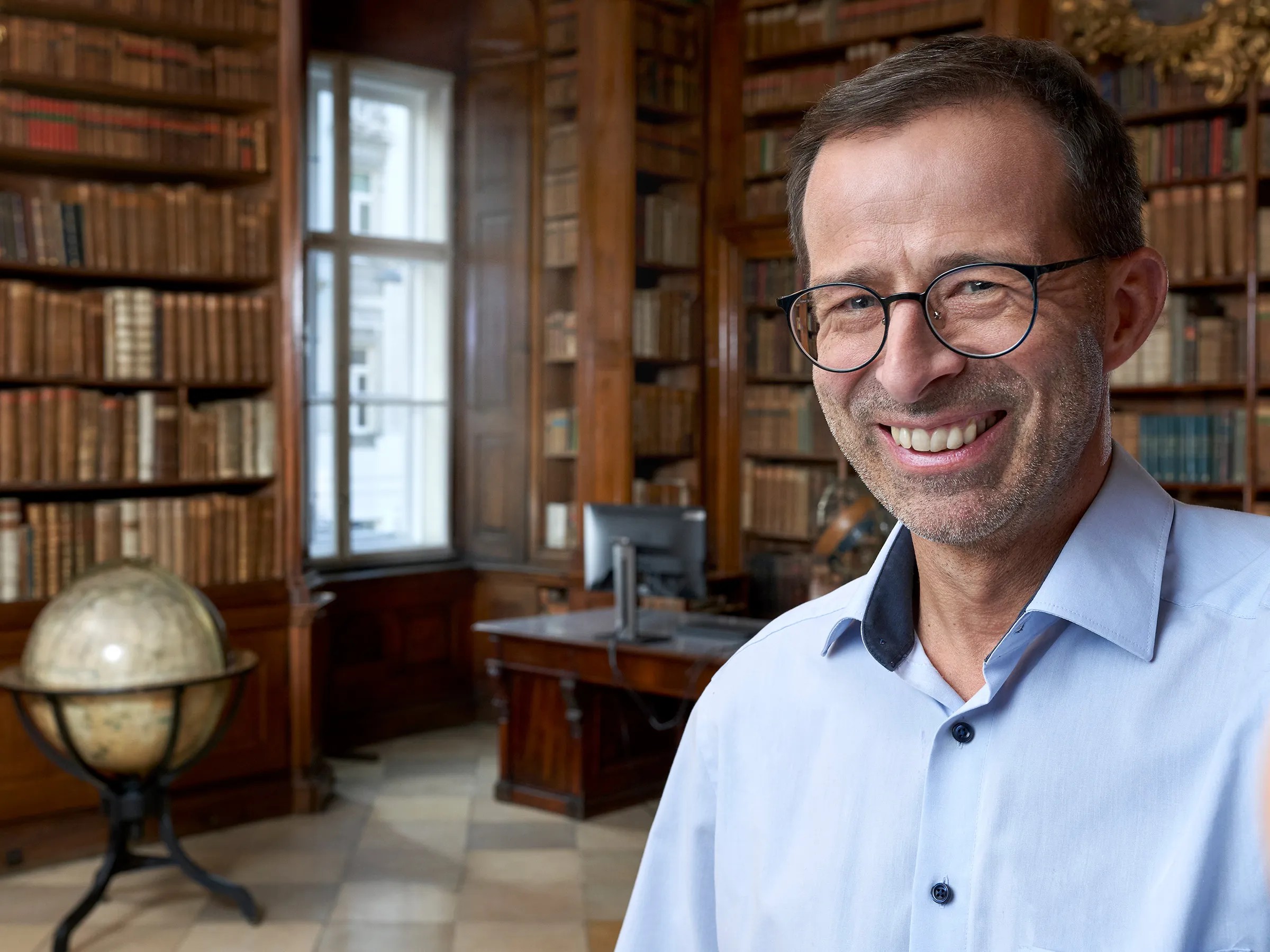 Ein lächelnder Mann mit Brille und blauem Hemd macht ein Selfie in der Bibliotheca Theresiana.