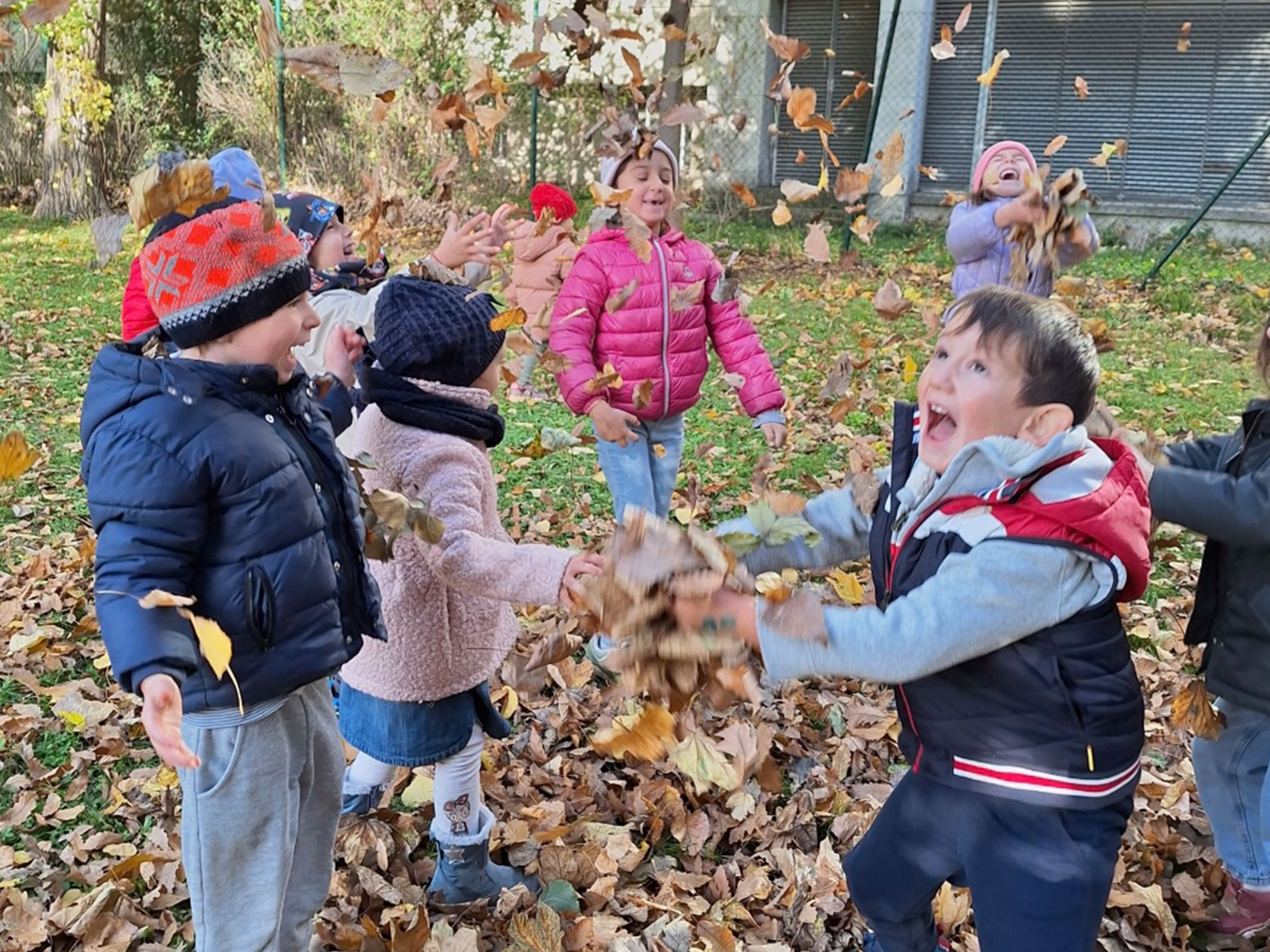 Gruppe von kleinen Kindern im Herbst mit den Blättern euphorisch spielend.