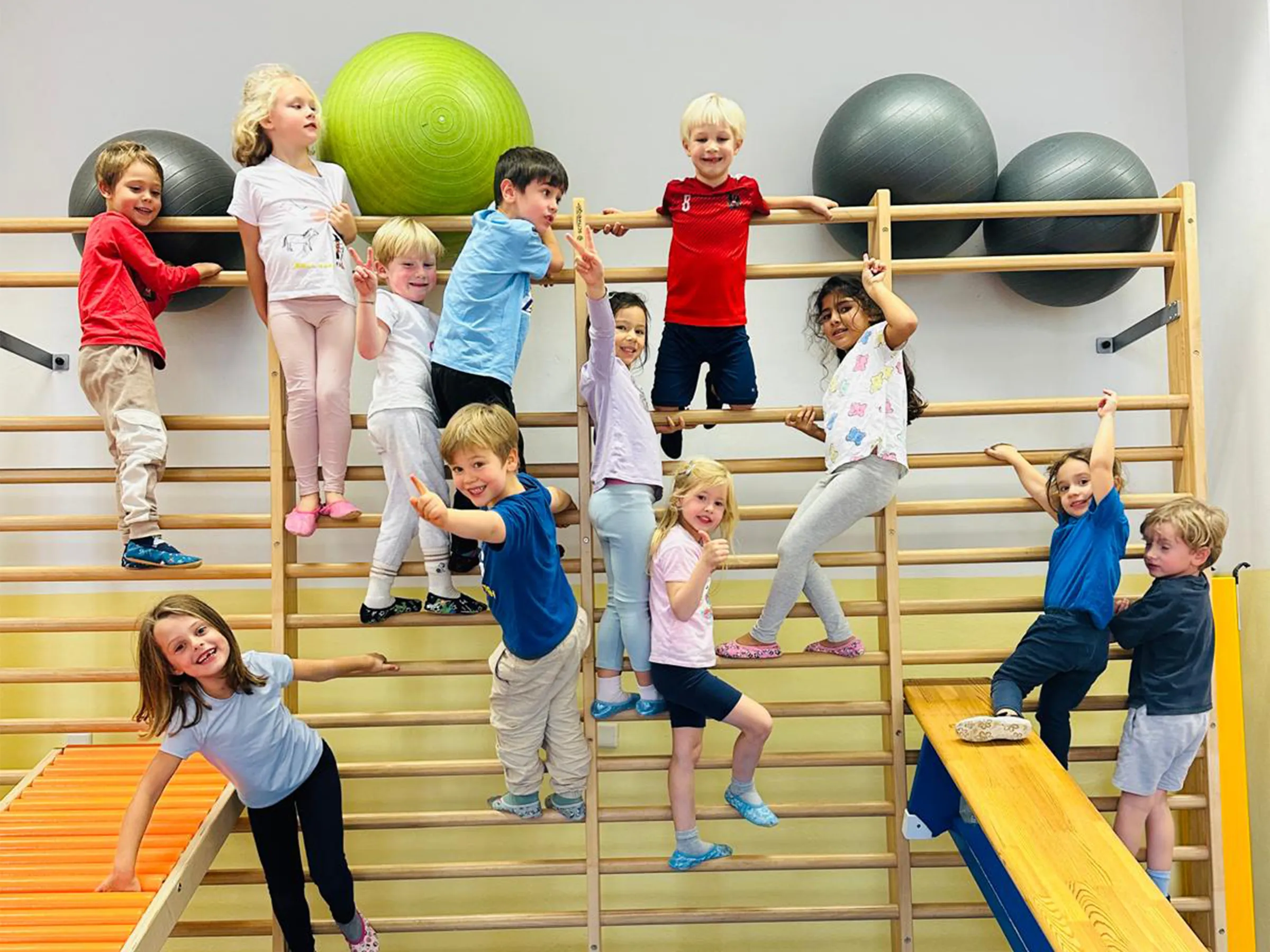 Gruppe von Kindern fröhlich auf einer mehreren Sprossenwänden hängend und in die Kamera lachend und winkend.
