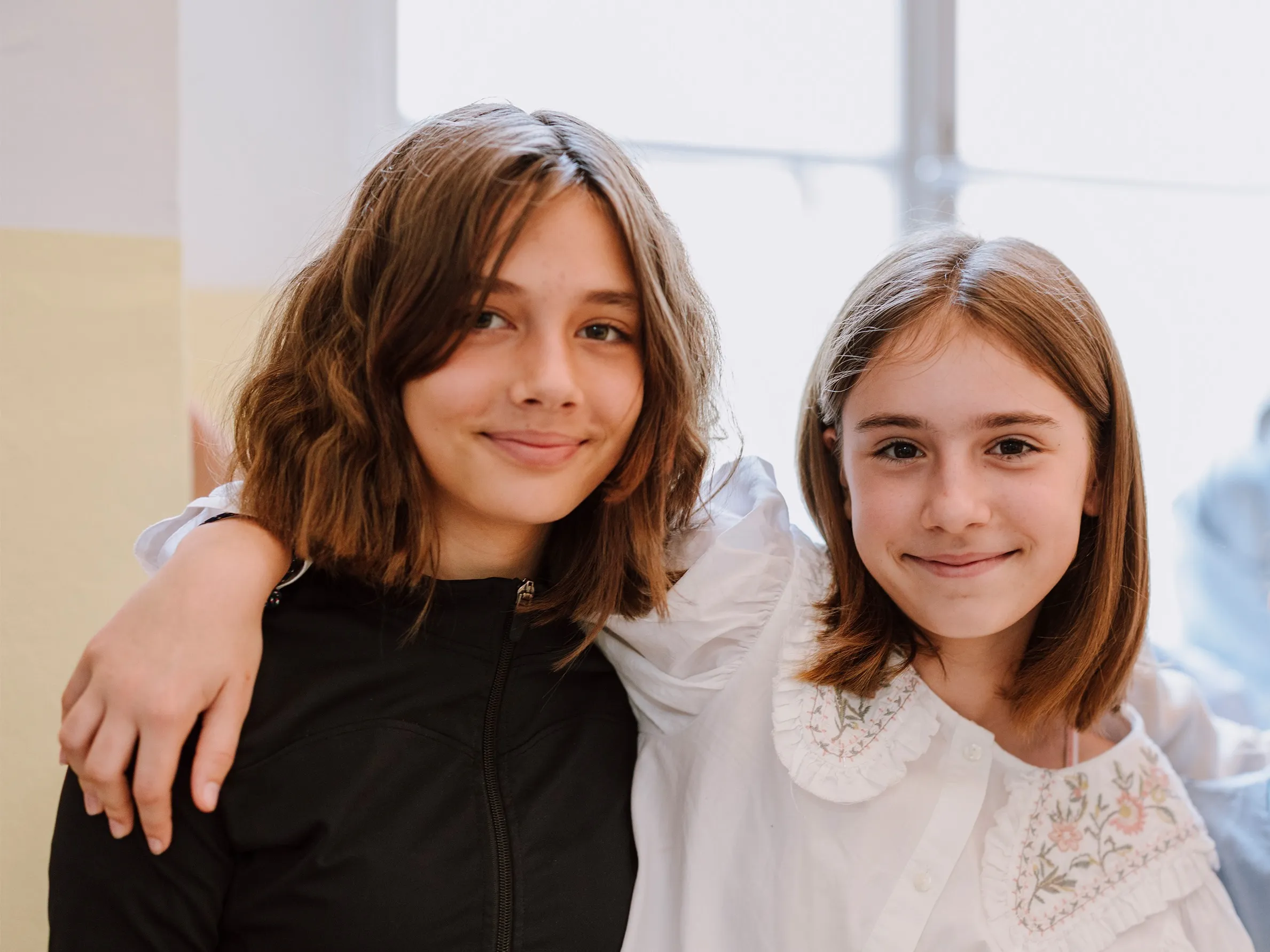 Zwei Maedchen mit brünetten Haaren sich umarmend und glücklich in die Kamera lachend.