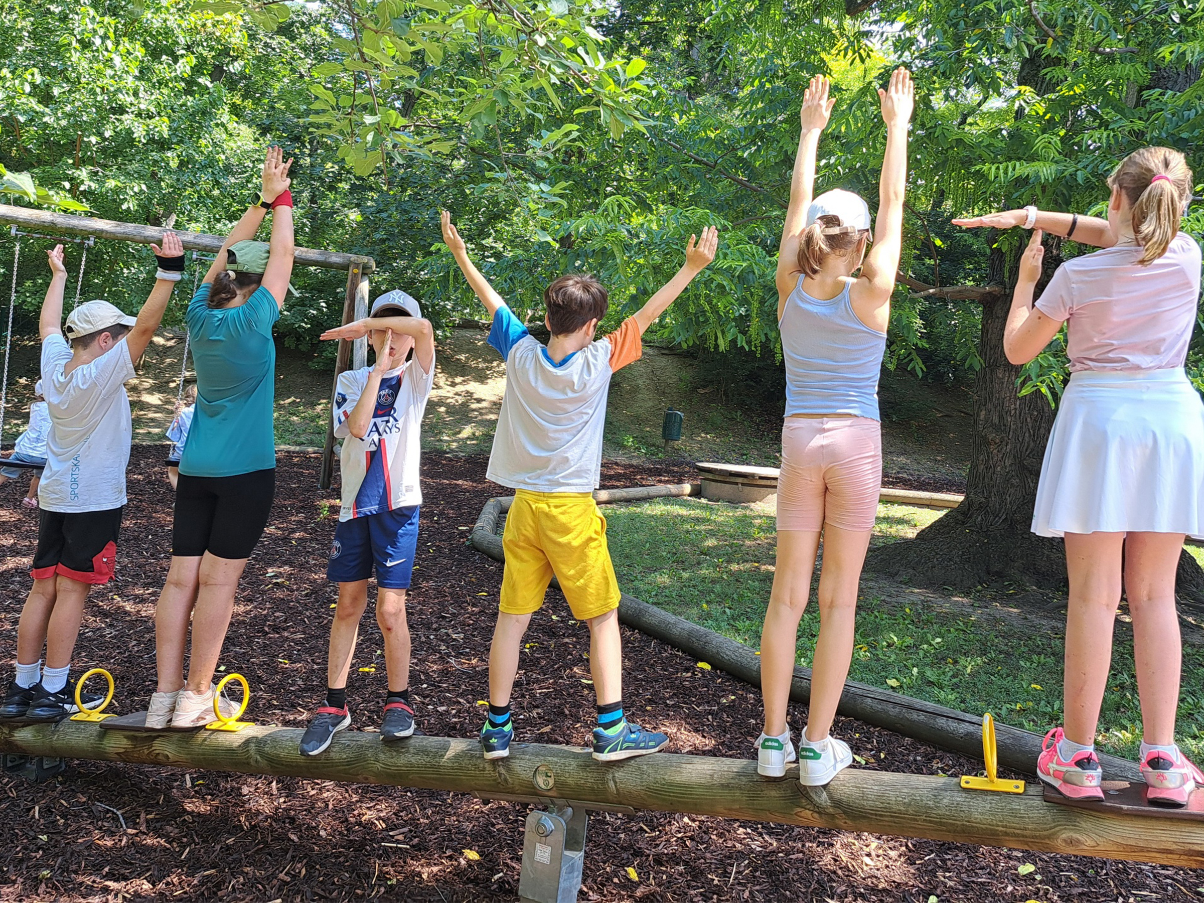 Kinder auf einem Baumstamm stehend von hinten zu sehen mit bunter Sommerkleidung