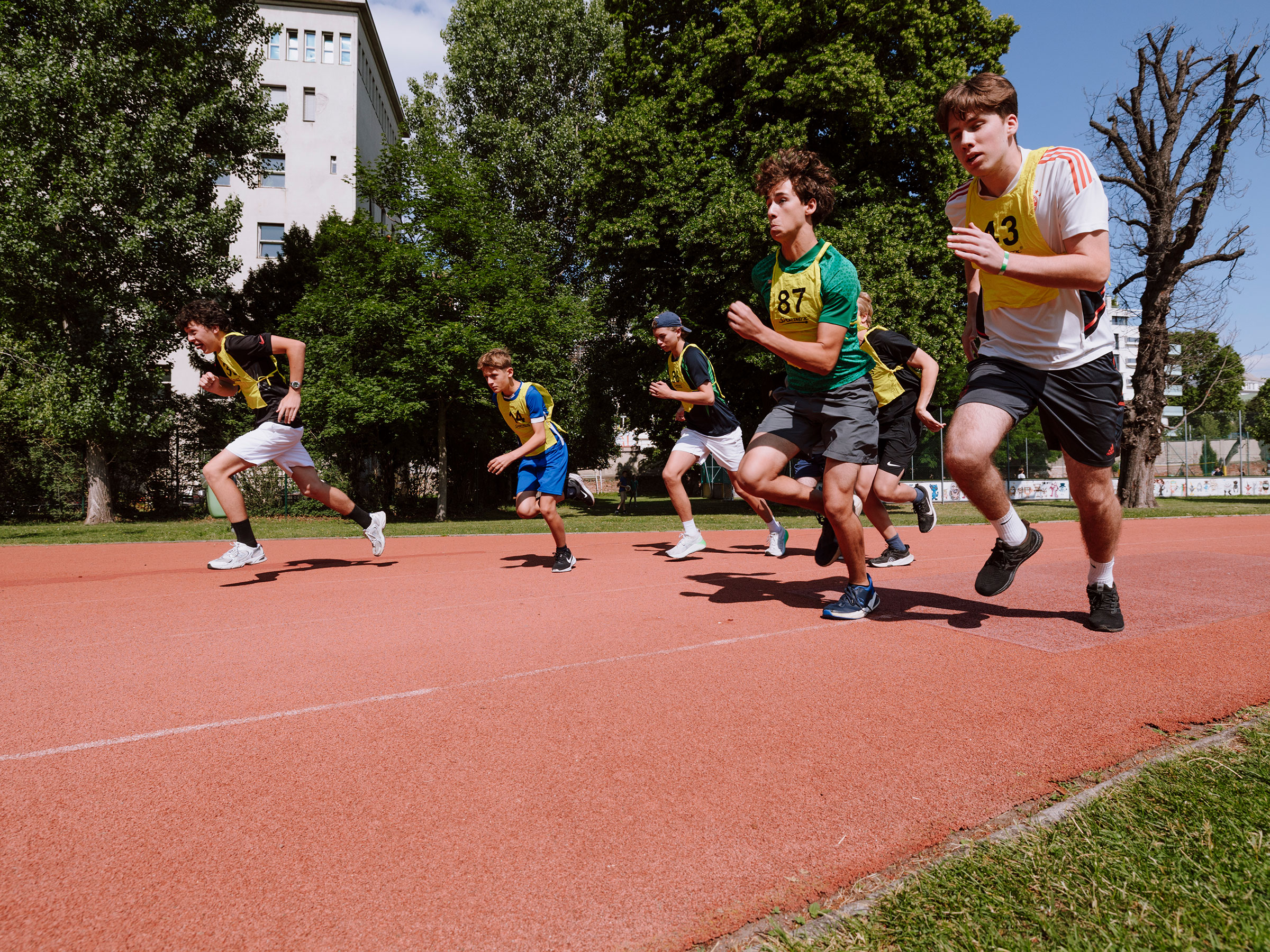 Gruppe von Burschen mit Startnummern bei sommerlichen Wetter auf einer Laufbahn sprintend.