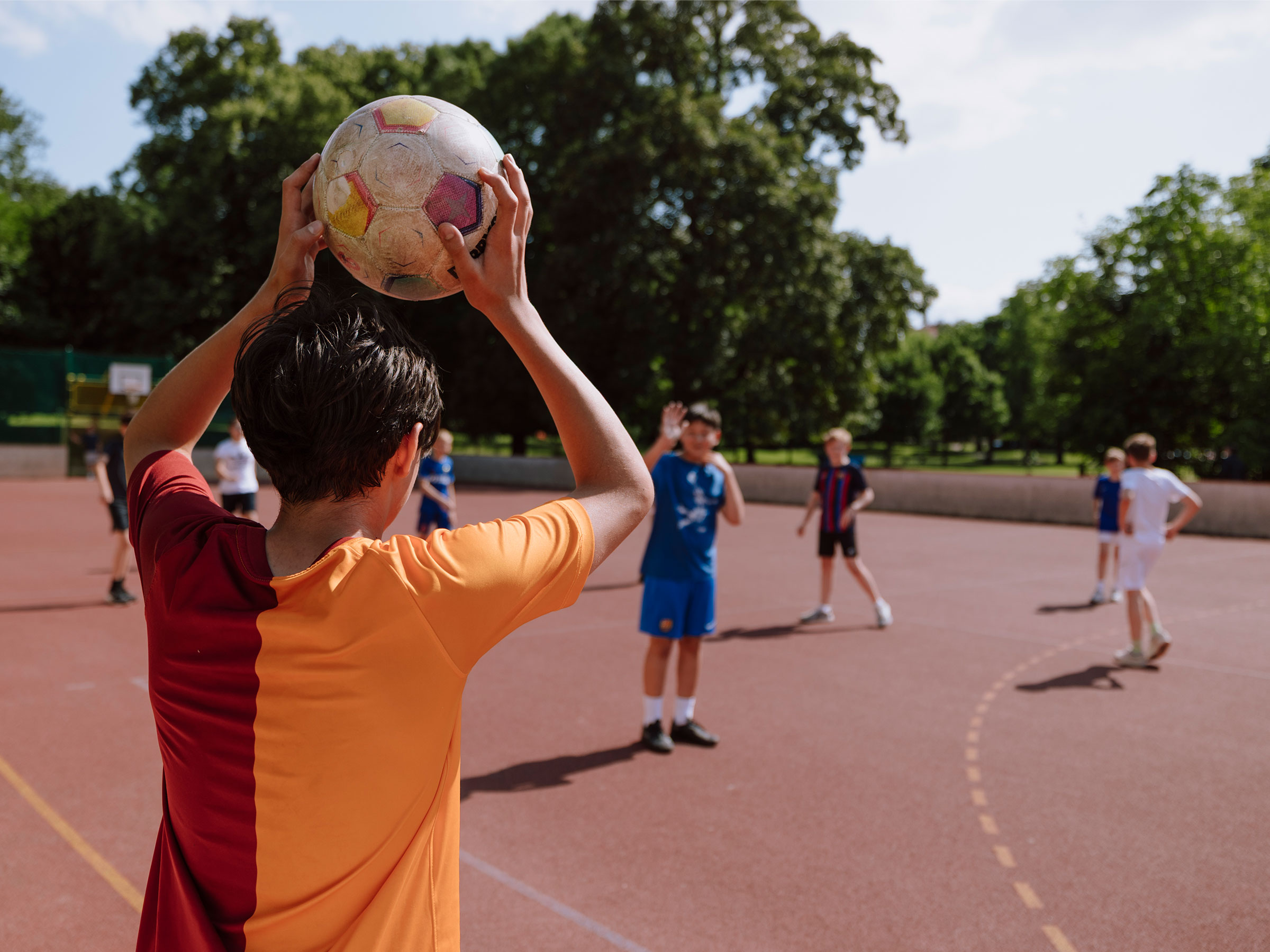 Bursche von hinten aufgenommen am Rande eines Funcourts einen Fußball vom Seitenaus einwerfend.