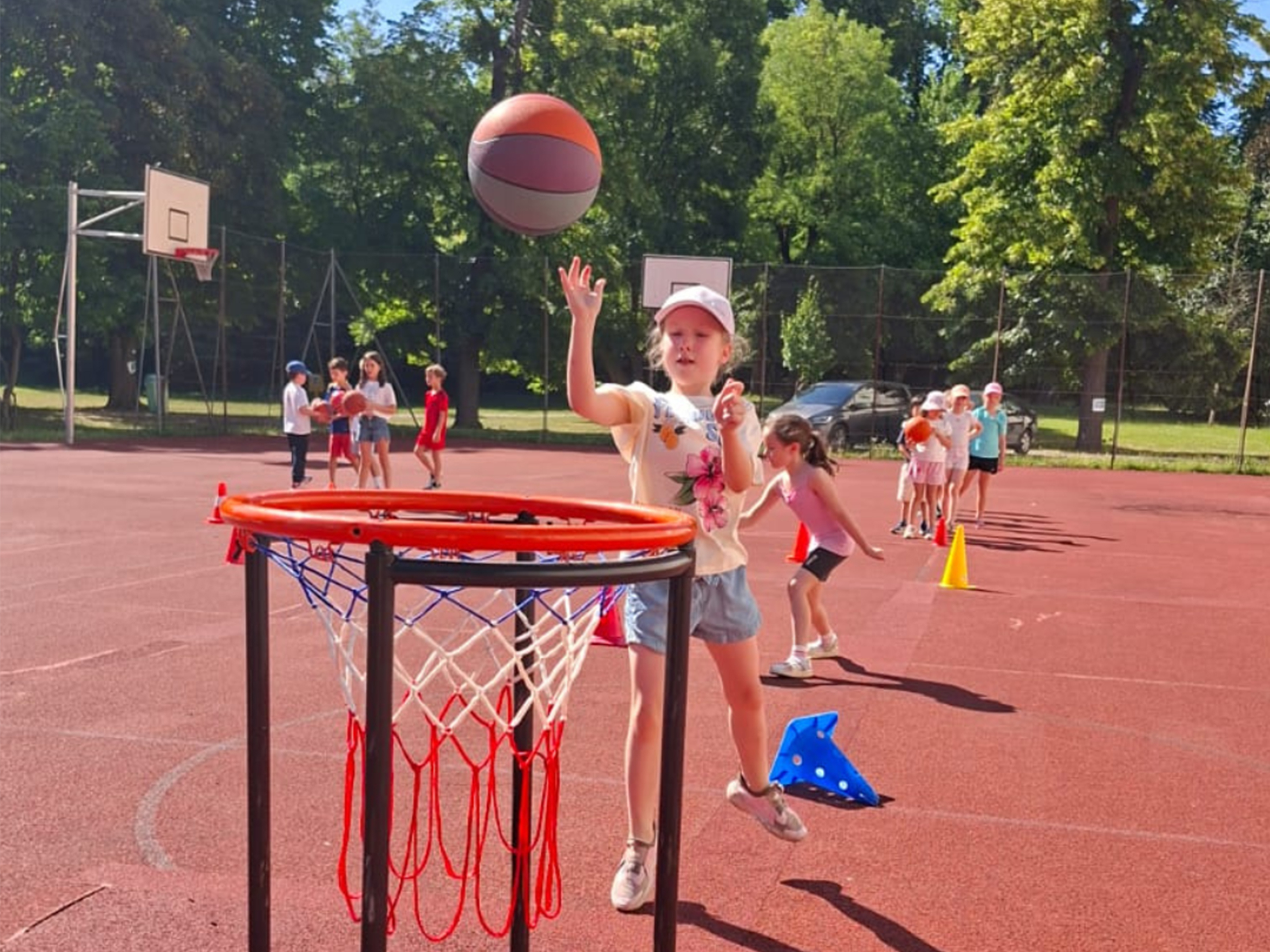 Junges Mädchen mit Baseballcap und Baskettball auf einem Funcourt den Ball in einen Korb werfendspielend