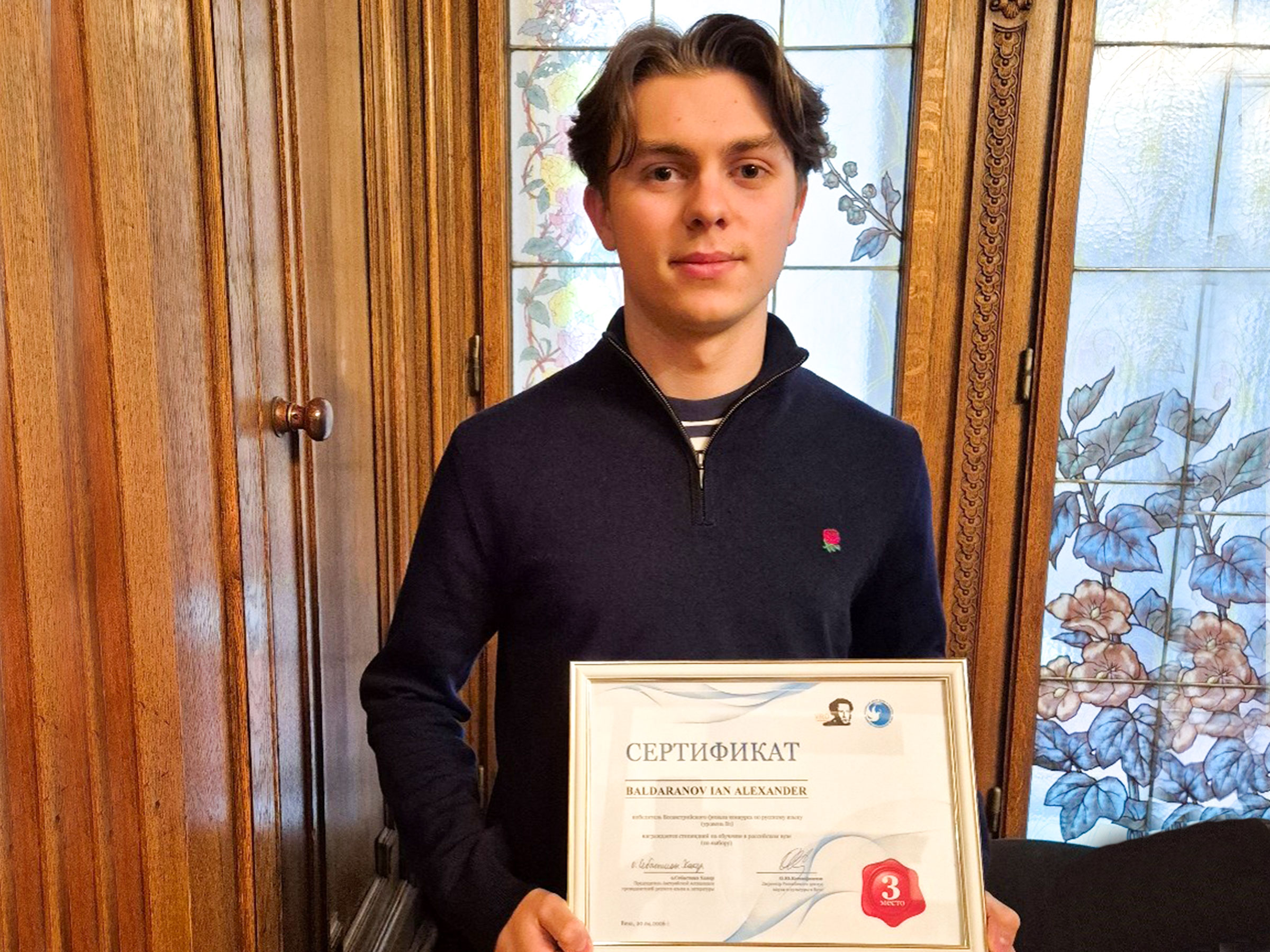 Junger Bursche mit brünetten Haaren hält ein Zertifikat erfreut in die Kamera