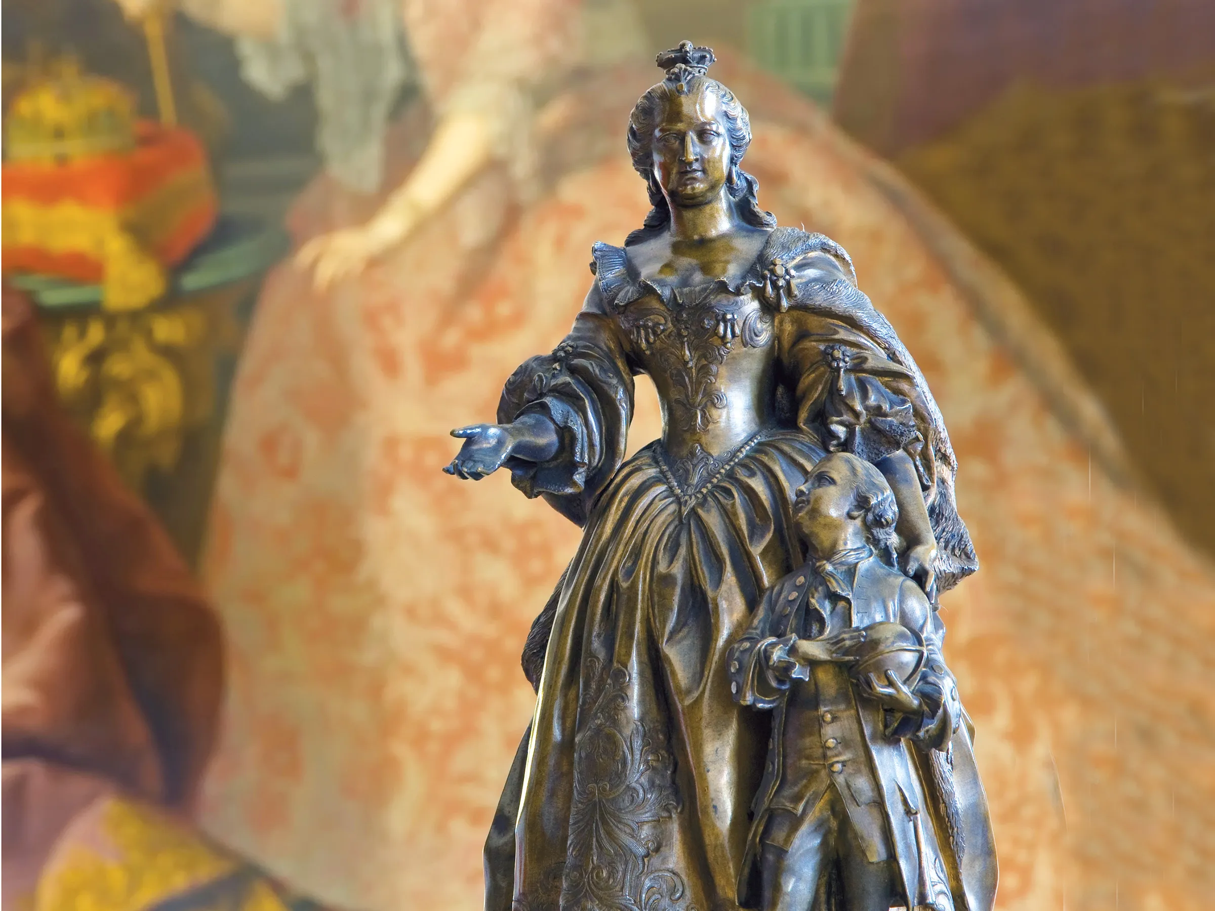 Bronzestatue einer Kaiserin mit einem Buben davor zur Kaiserin hochblickend vor einem Gemäldehintergrund.