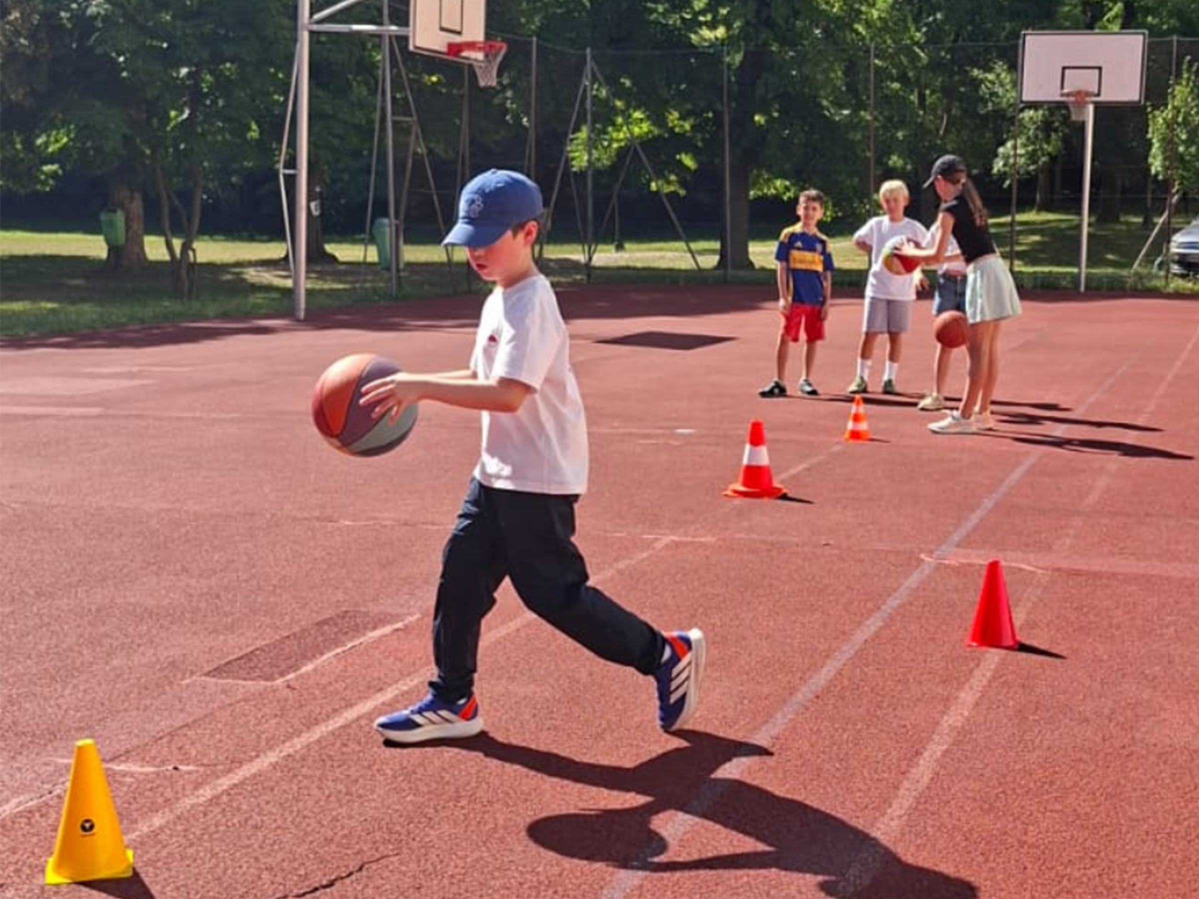 Junger Bursch mit blauem Cap und Baskettball auf einem Funcourt spielend