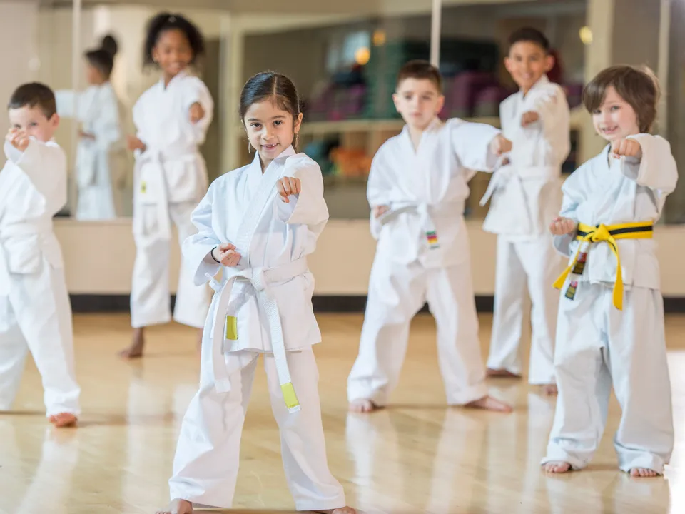 Gruppe von lachenden Kindern in Taekwondo Gewand, barfuß und mit Kampfpose in einem Turnsaal