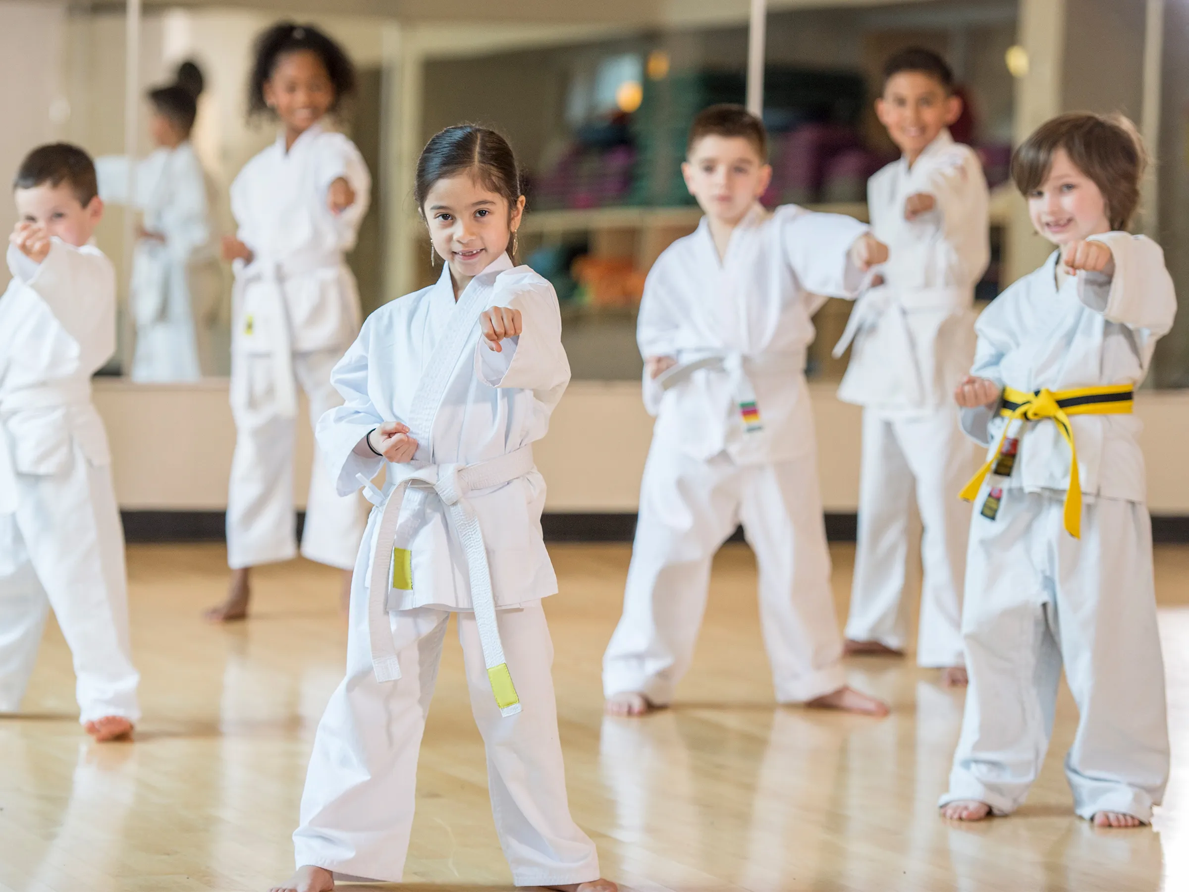 Gruppe von lachenden Kindern in Taekwondo Gewand, barfuß und mit Kampfpose in einem Turnsaal