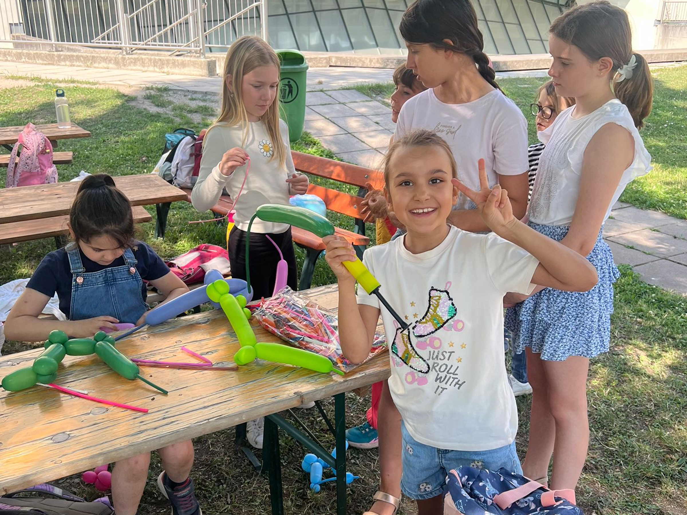Mädchengruppe auf einer Bank im Freien mit Lufballons am einem Sommertag spielend