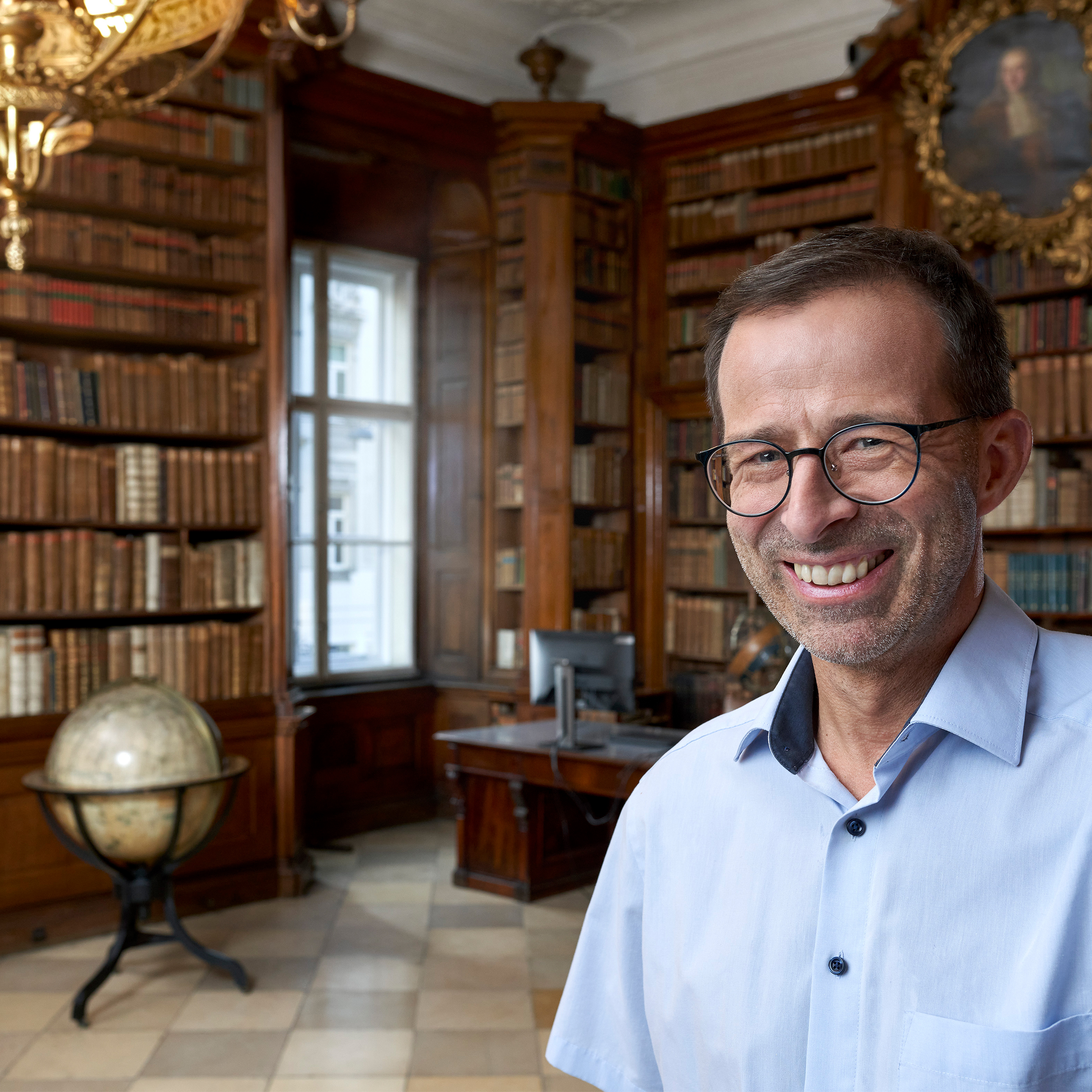 Ein lächelnder Mann mit Brille und blauem Hemd macht ein Selfie in der Bibliotheca Theresiana.