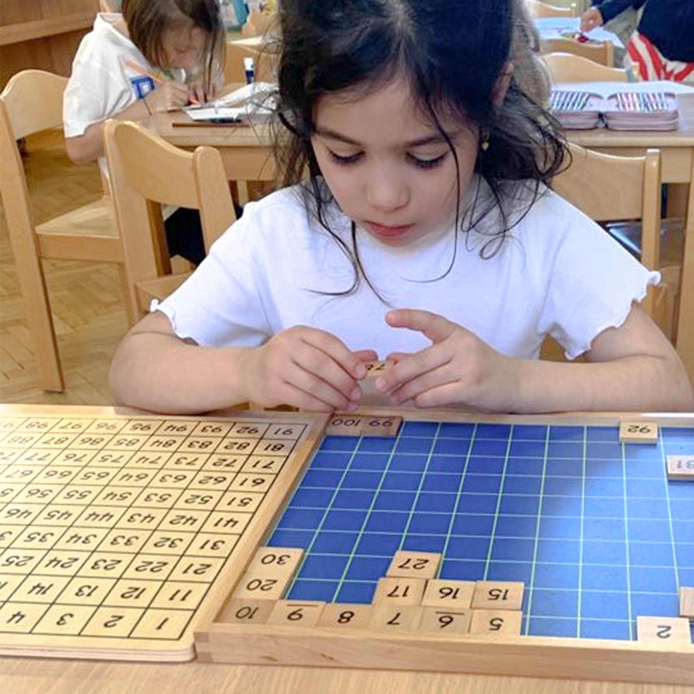 Mädchen mit dunklen Haaren vertieft mit einem Art Schachbrett voller Zahlen arbeitend.